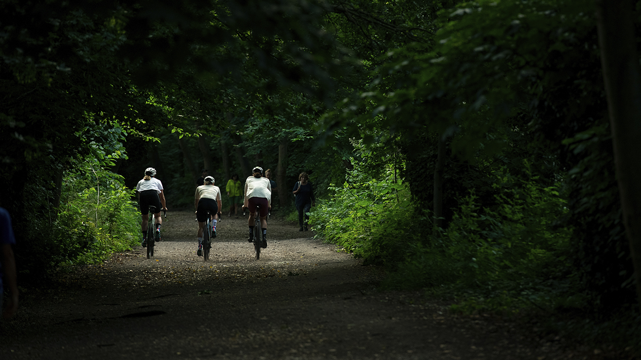 Two women and one man cycle down a gravel path in a forest