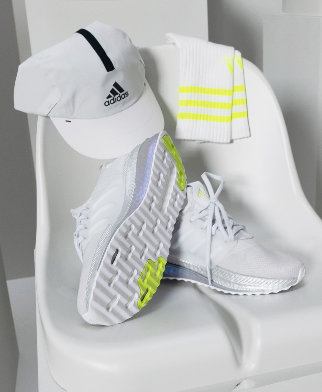 A close-up photo X_PLRBOOST trainers, cap and socks from the adidas Z.N.E. Sportswear collection displayed on a plastic football stadium seat.