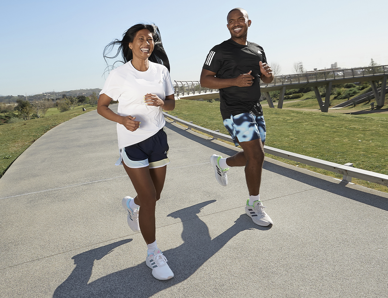 A man and women run through the park whilst laughing together.