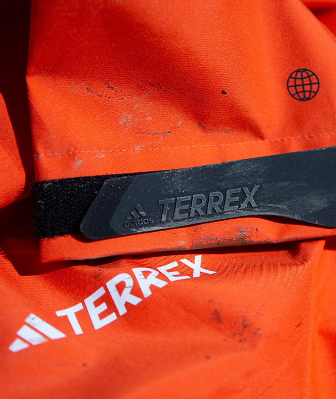 Primer plano de una chaqueta de GORE-TEX naranja adidas TERREX con manchas de barro en la manga.