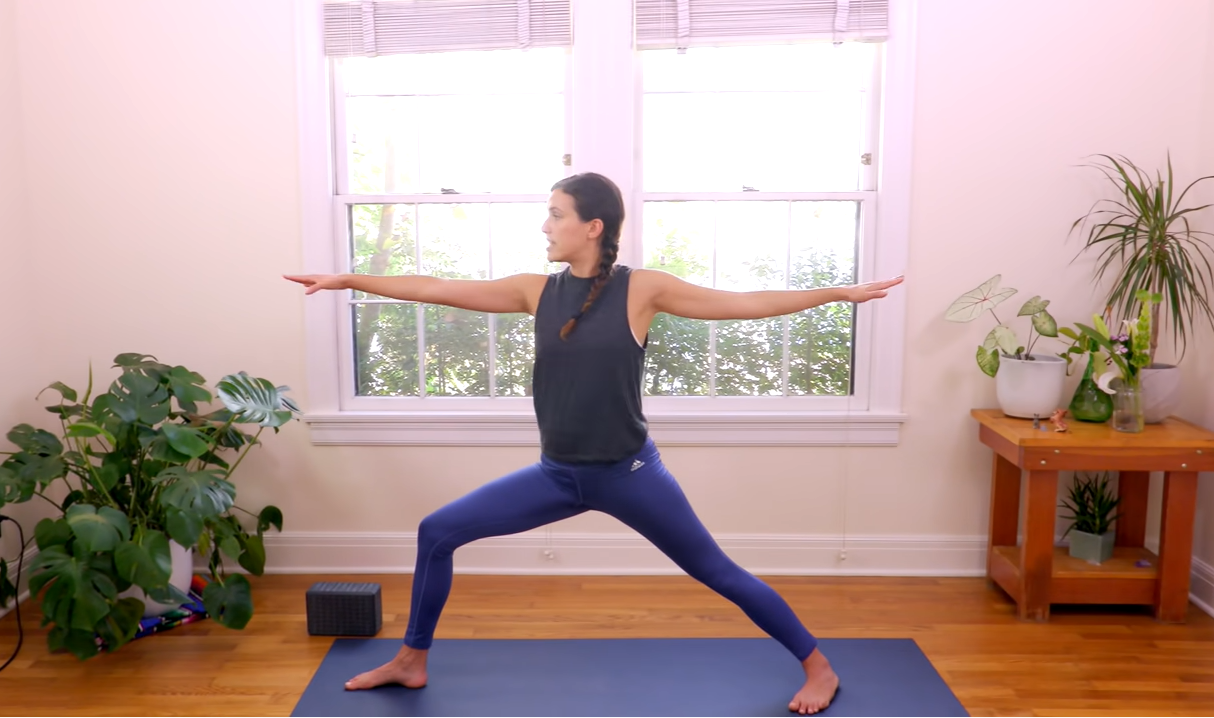 How-To-Start-Yoga-BodyImage-6 Framed by plants, Adriene is seen in her studio holding the warrior II pose.