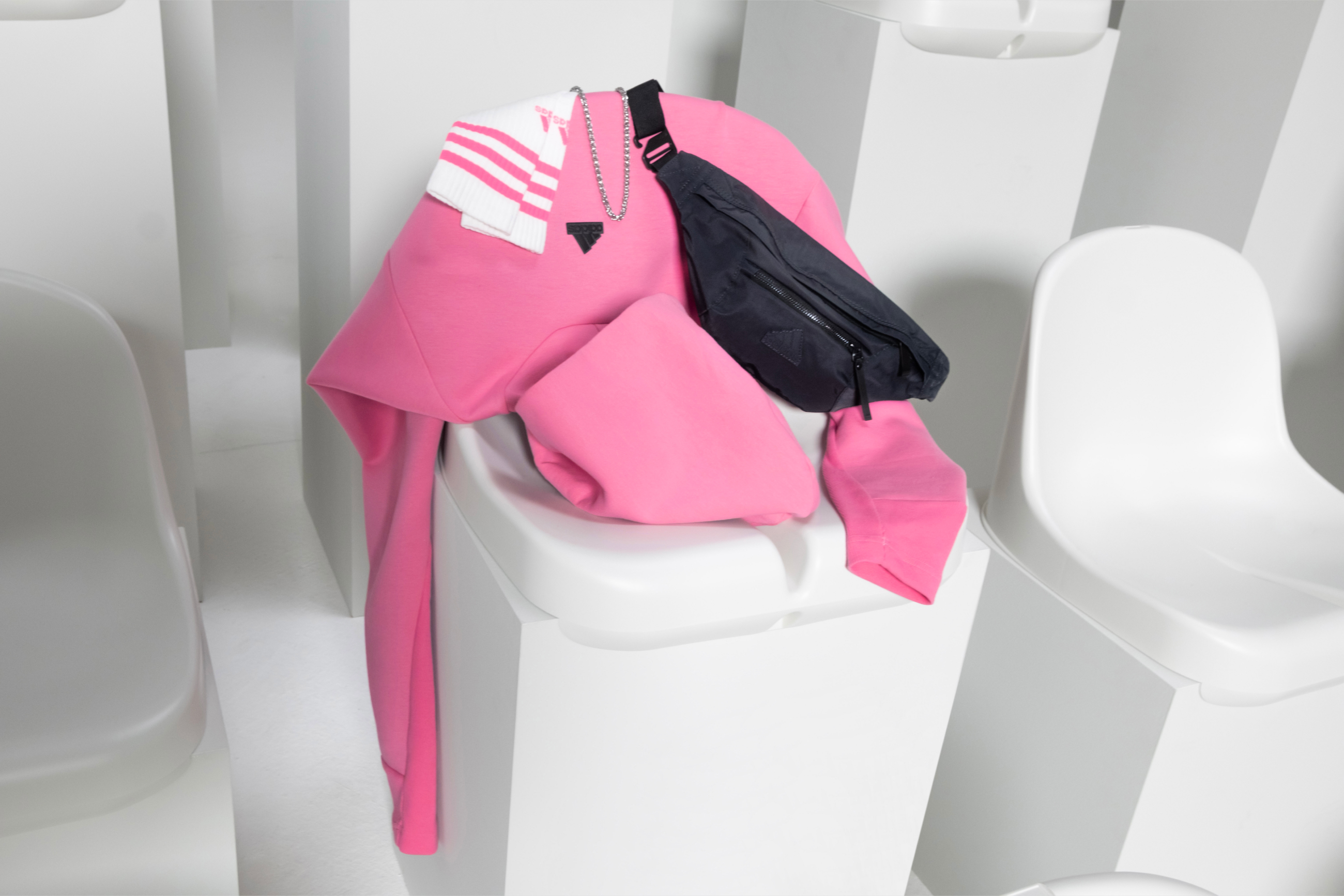 Zdjęcie bluzy z kapturem, torebki na pasku oraz skarpetek z kolekcji ubrań sportowych adidas Z.N.E. w aranżacji na plastikowym siedzeniu na trybunach stadionu.