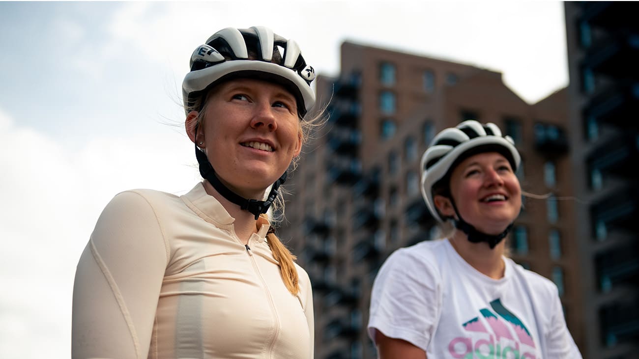 fw21-cycling-mental-health-blog-body-4 Zwei Frauen mit Fahrradhelm in städtischer Umgebung