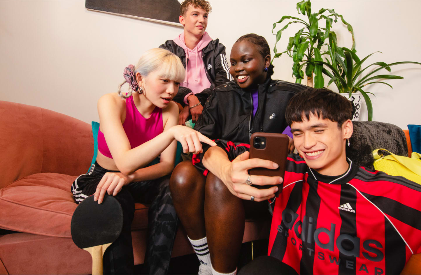 sportswear-SS23-global-launch-sportswear-blogpost-image1-d Vier lächelnde Personen auf einer Couch, die auf ein Handy schauen und auf den Bildschirm zeigen.