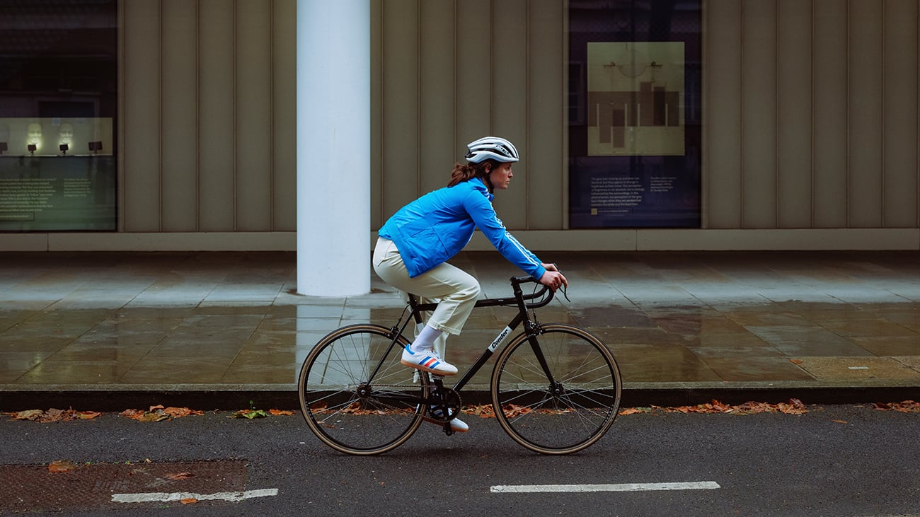 A women cycles centre frame through the rain of a city street.
