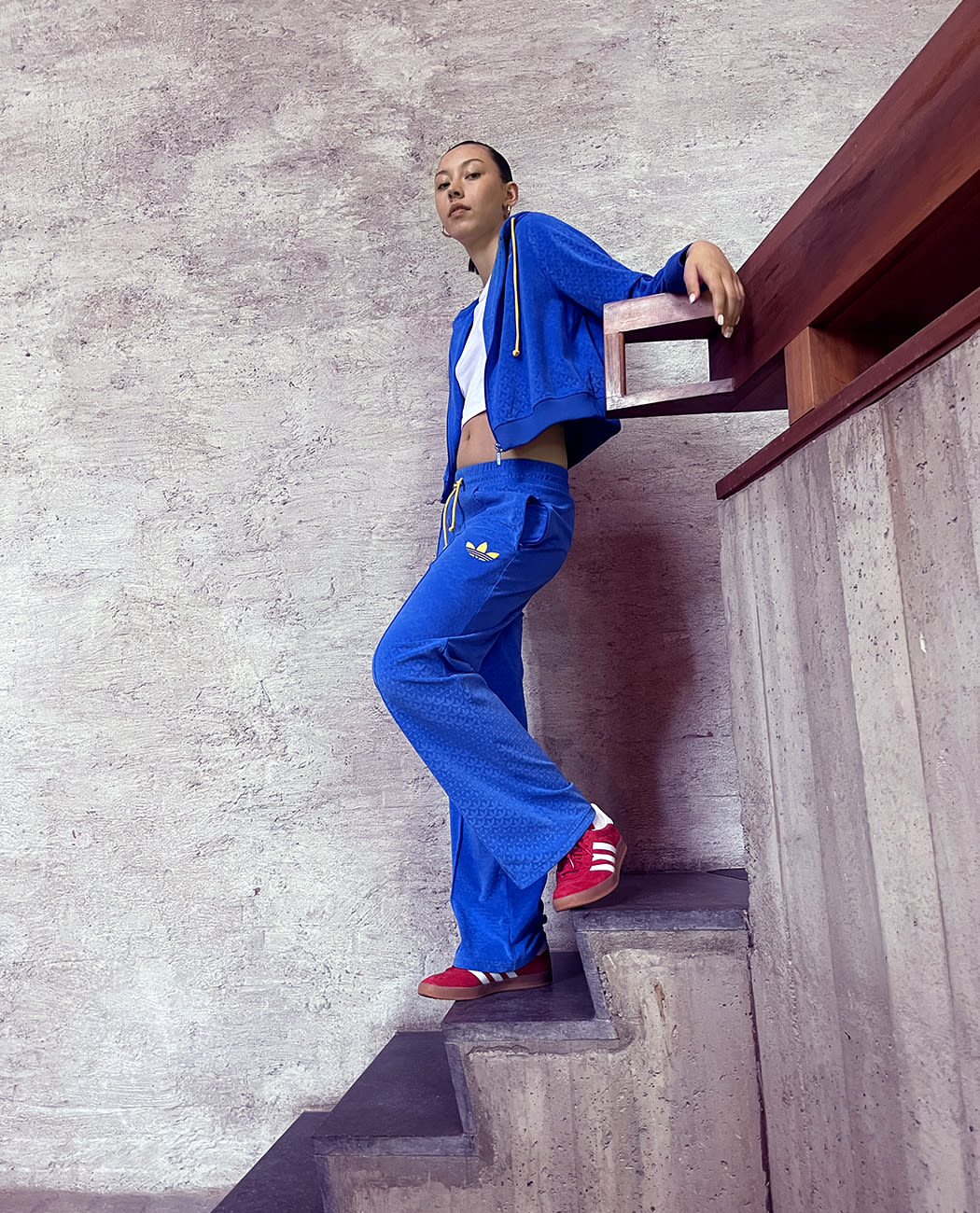 Female model standing on a flight of stairs wearing a blue outfit  on a white t-shirt and red adidas Gazelle sneakers with with stripes.