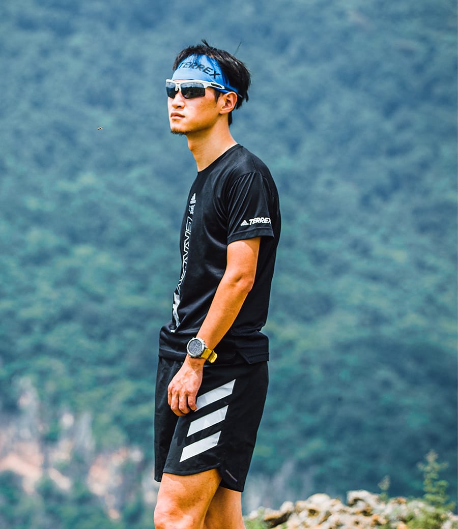 Chinese trail runner in black stands on a hillside looking in to the distance