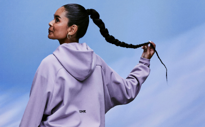 A woman with black hair in a braid wears a purple adidas Z.N.E. hoodie in front of a light blue backdrop.