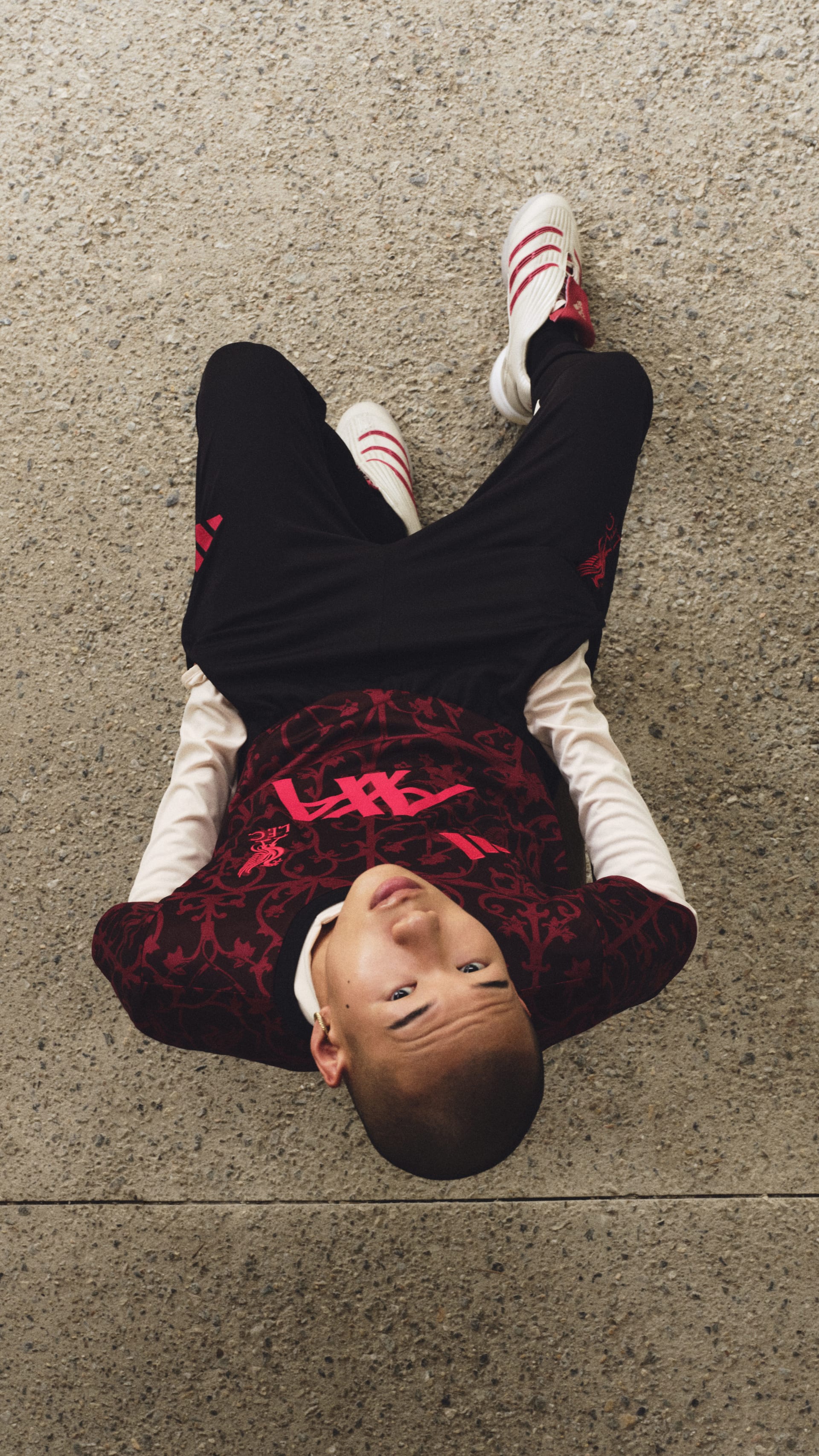 A person wearing a black outfit with red patterns is lying on a carpeted floor, their eyes closed.