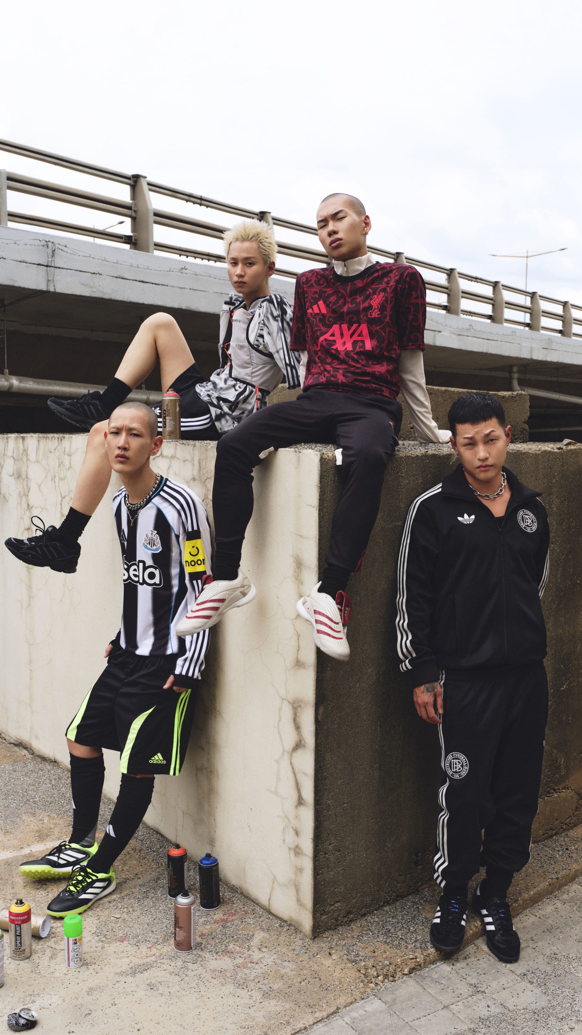 The image shows a group of young people, likely friends, sitting on a concrete structure in an urban setting. They appear to be wearing casual clothing, including sports jerseys and jackets, and are engaged in some kind of social activity or interaction.