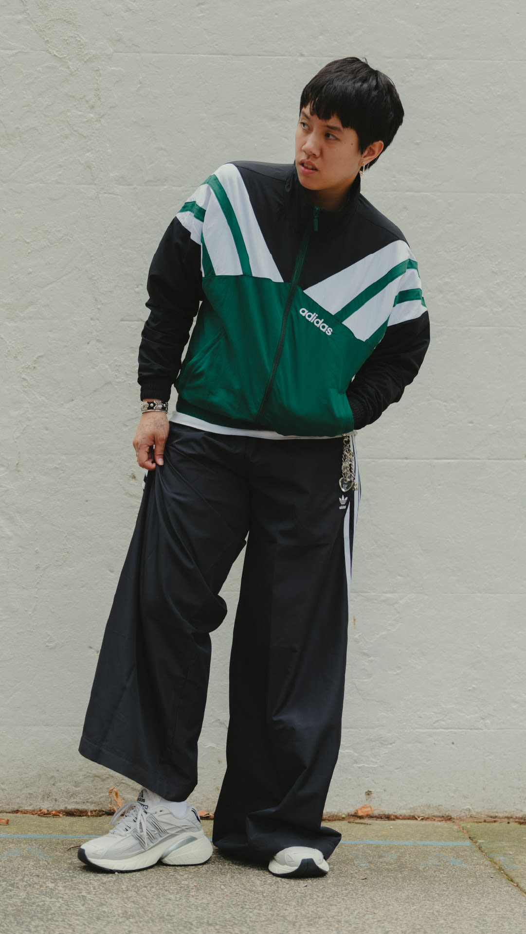A young person wearing an Adidas tracksuit stands in front of a plain white wall.