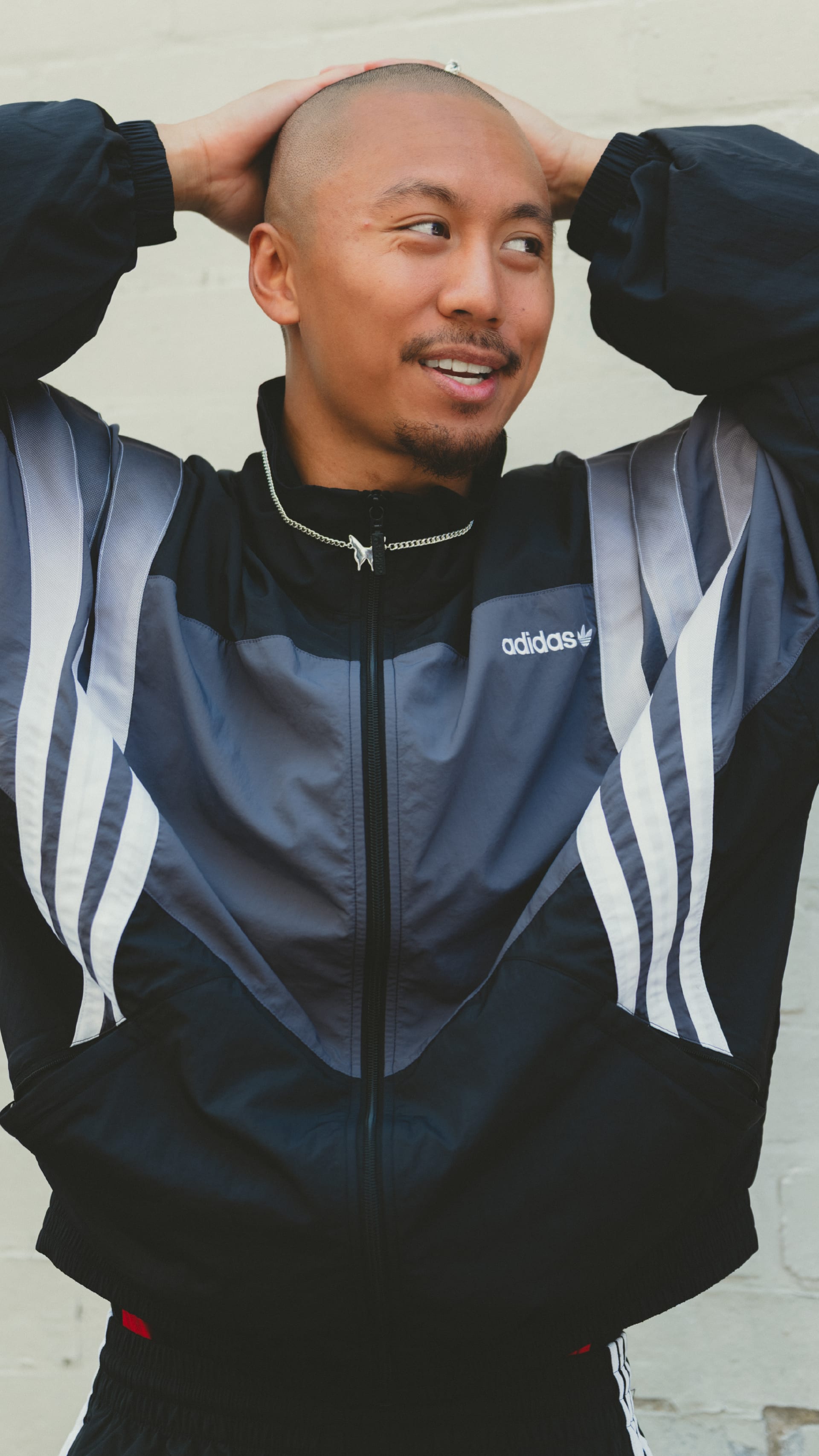 A smiling man wearing an Adidas tracksuit jacket stands against a plain white background.