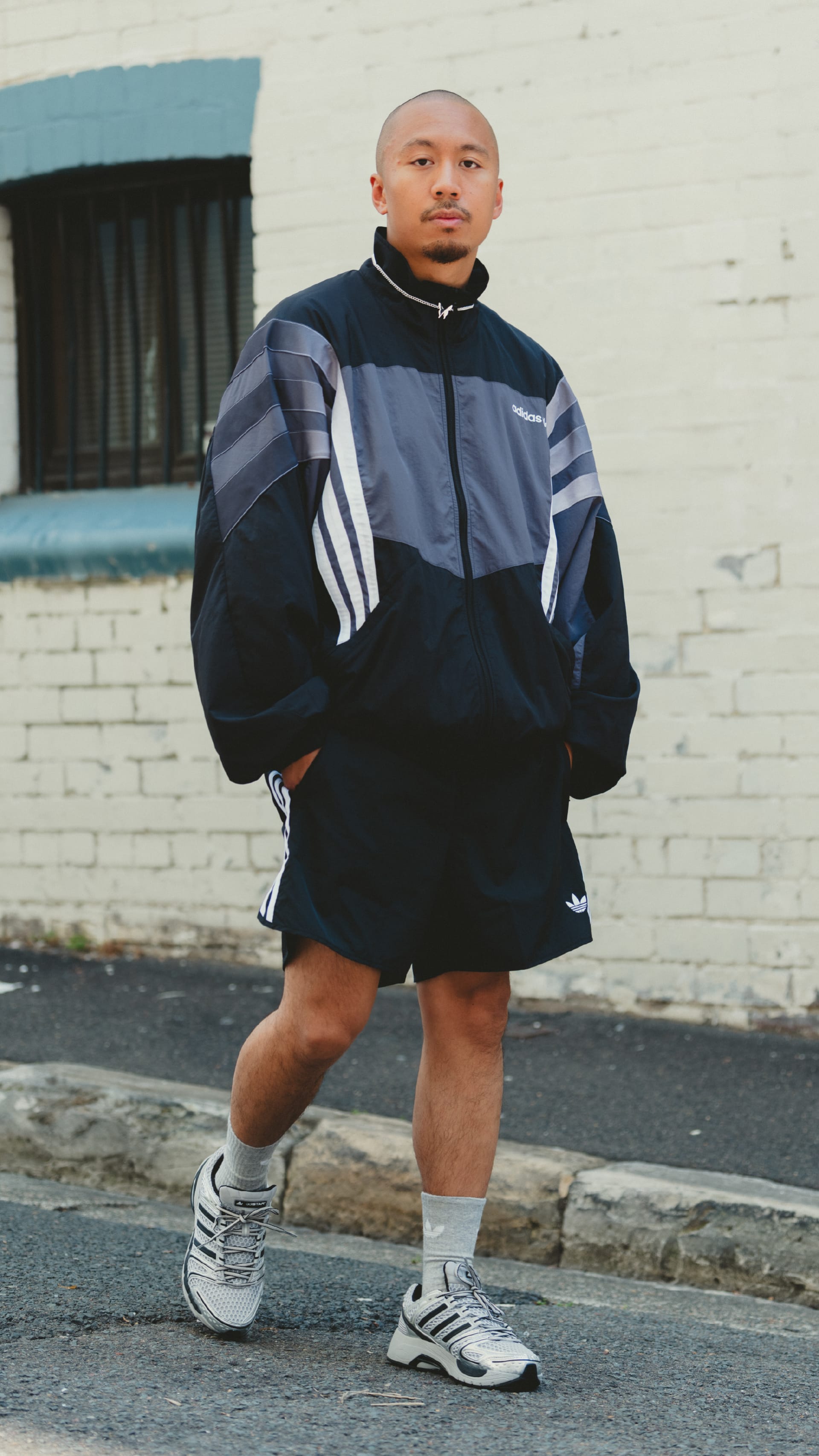 A person wearing a colorful jacket and shorts stands on a paved street in front of a brick building.