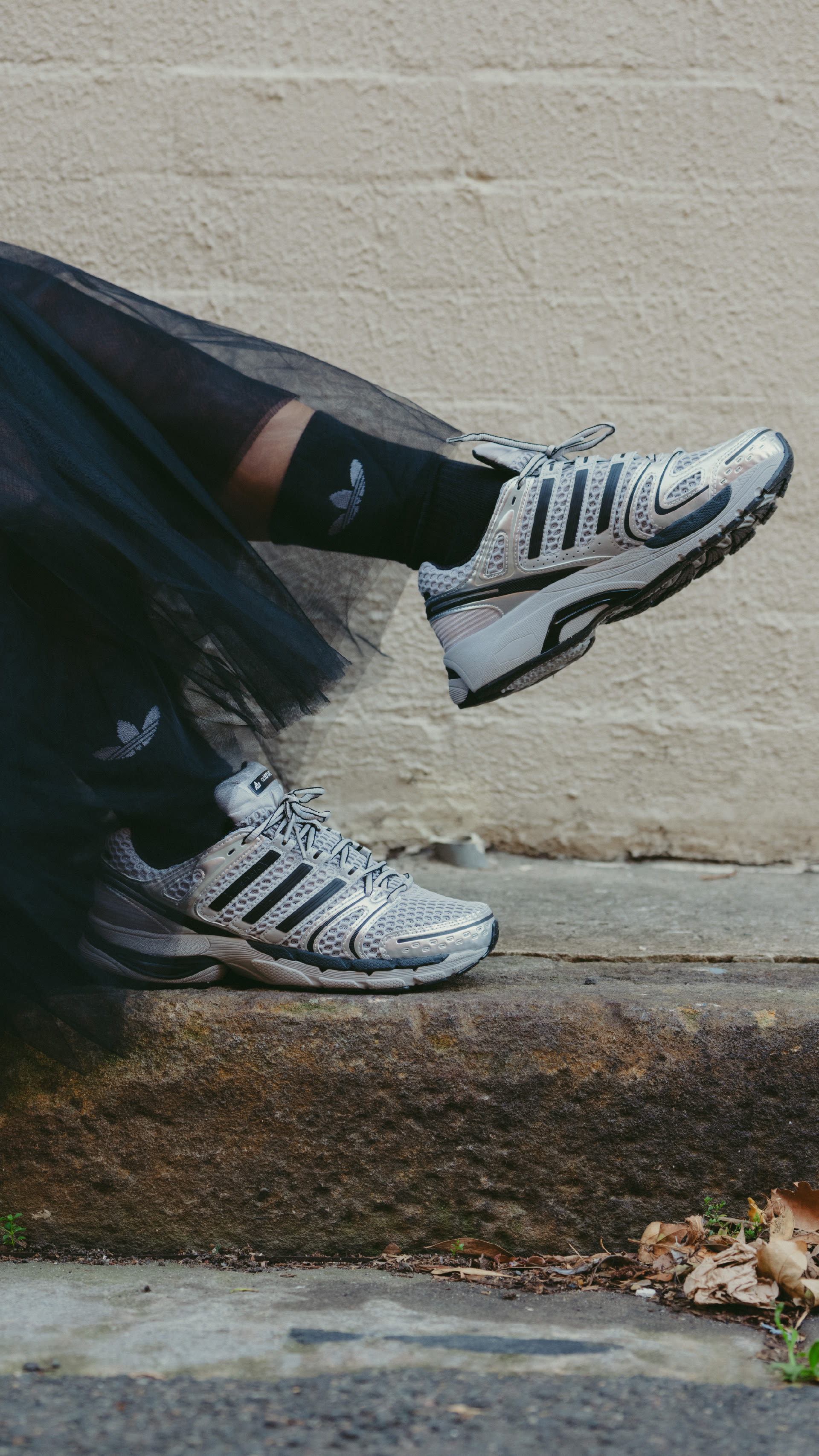 The image shows a pair of athletic shoes on a wooden surface, with a brick wall in the background.