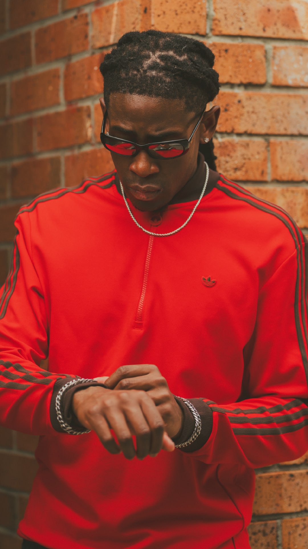 A young person wearing a bright red shirt and sunglasses stands in front of a brick wall.