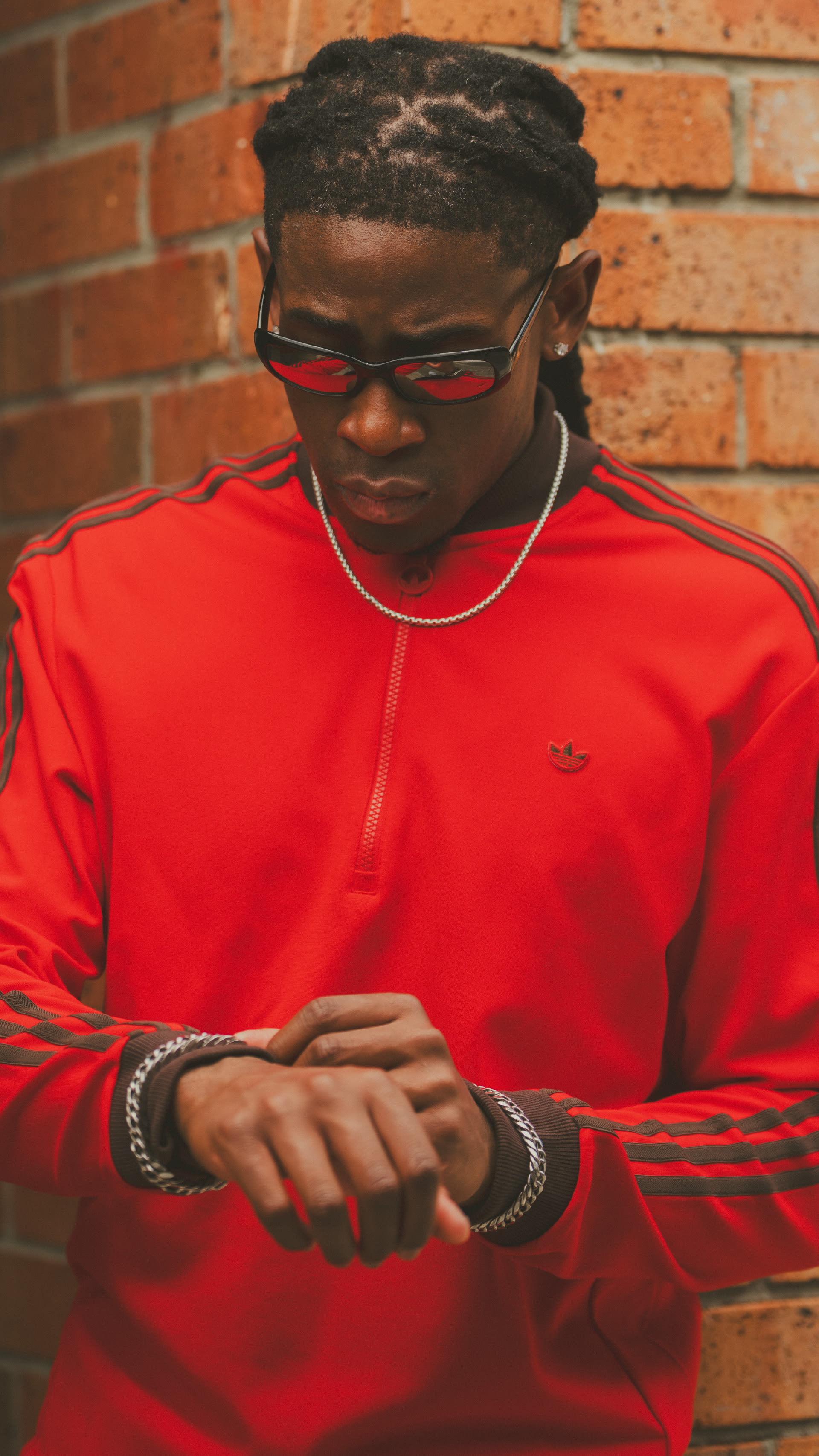 A person wearing a red shirt and sunglasses stands in front of a brick wall.