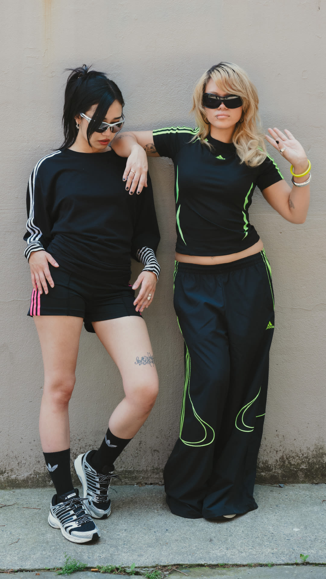 Two women wearing matching black and green athletic outfits are posing together against a plain white wall.
