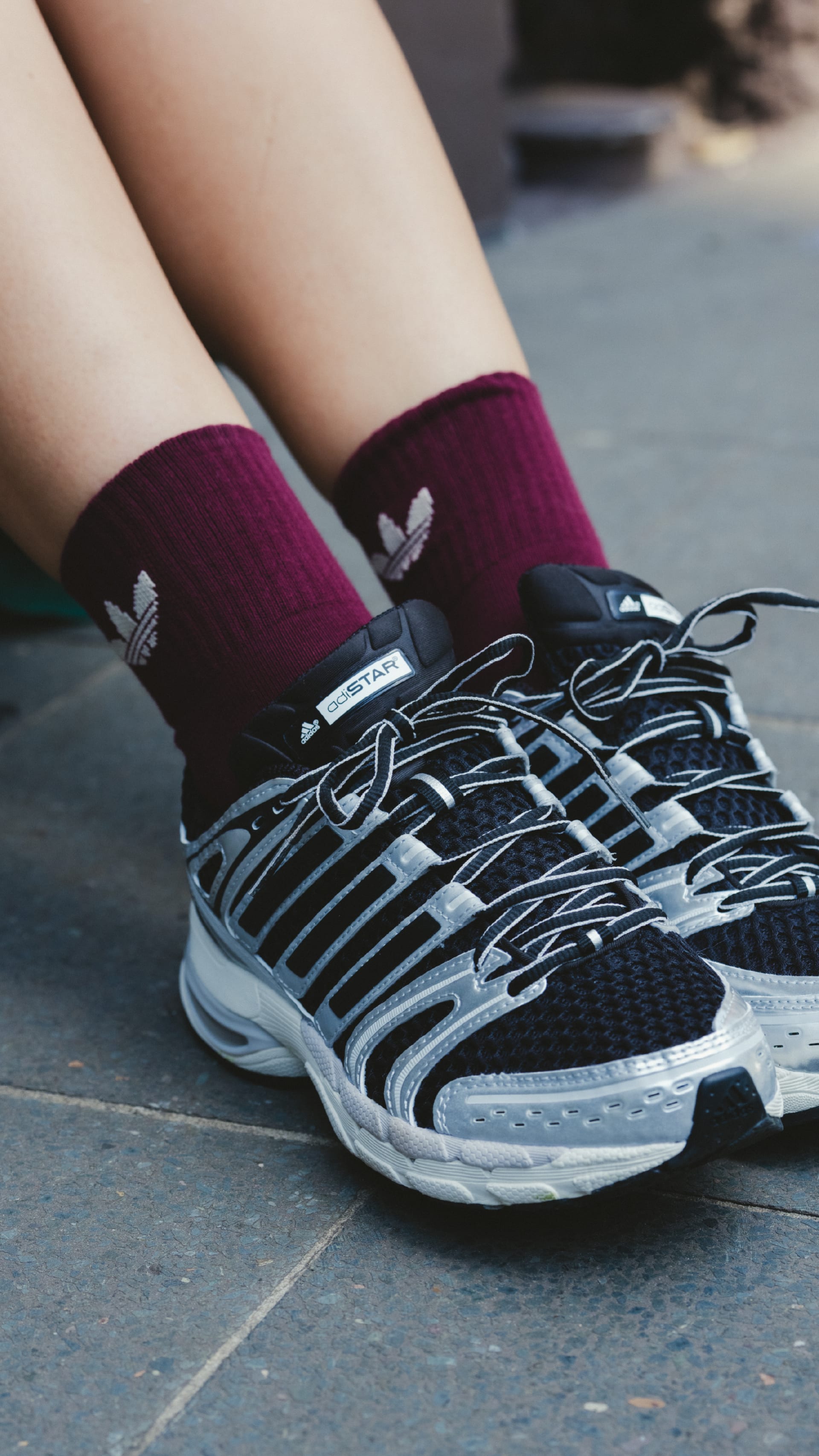 The image shows a pair of feet wearing black and white athletic shoes with purple socks, standing on a tiled floor.