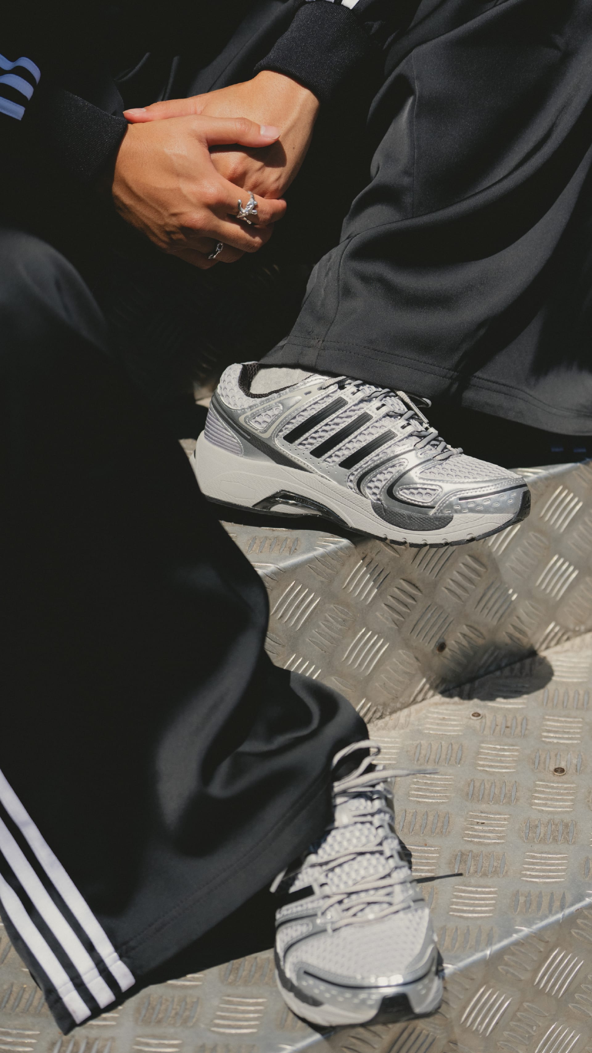 The image shows a person's lower body wearing a dark suit and a pair of white sneakers standing on a checkered floor.