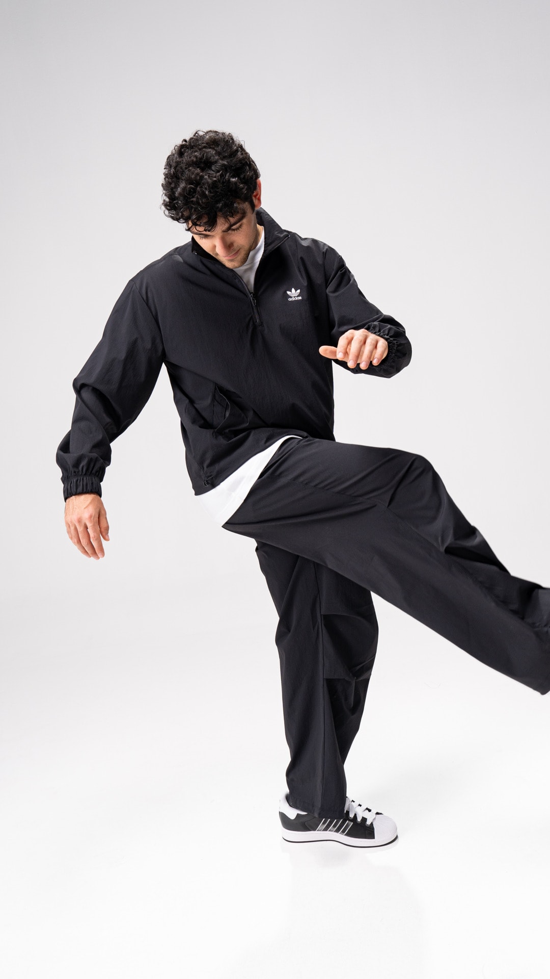 A person wearing a black outfit is performing a dynamic martial arts move, with a plain white background.
