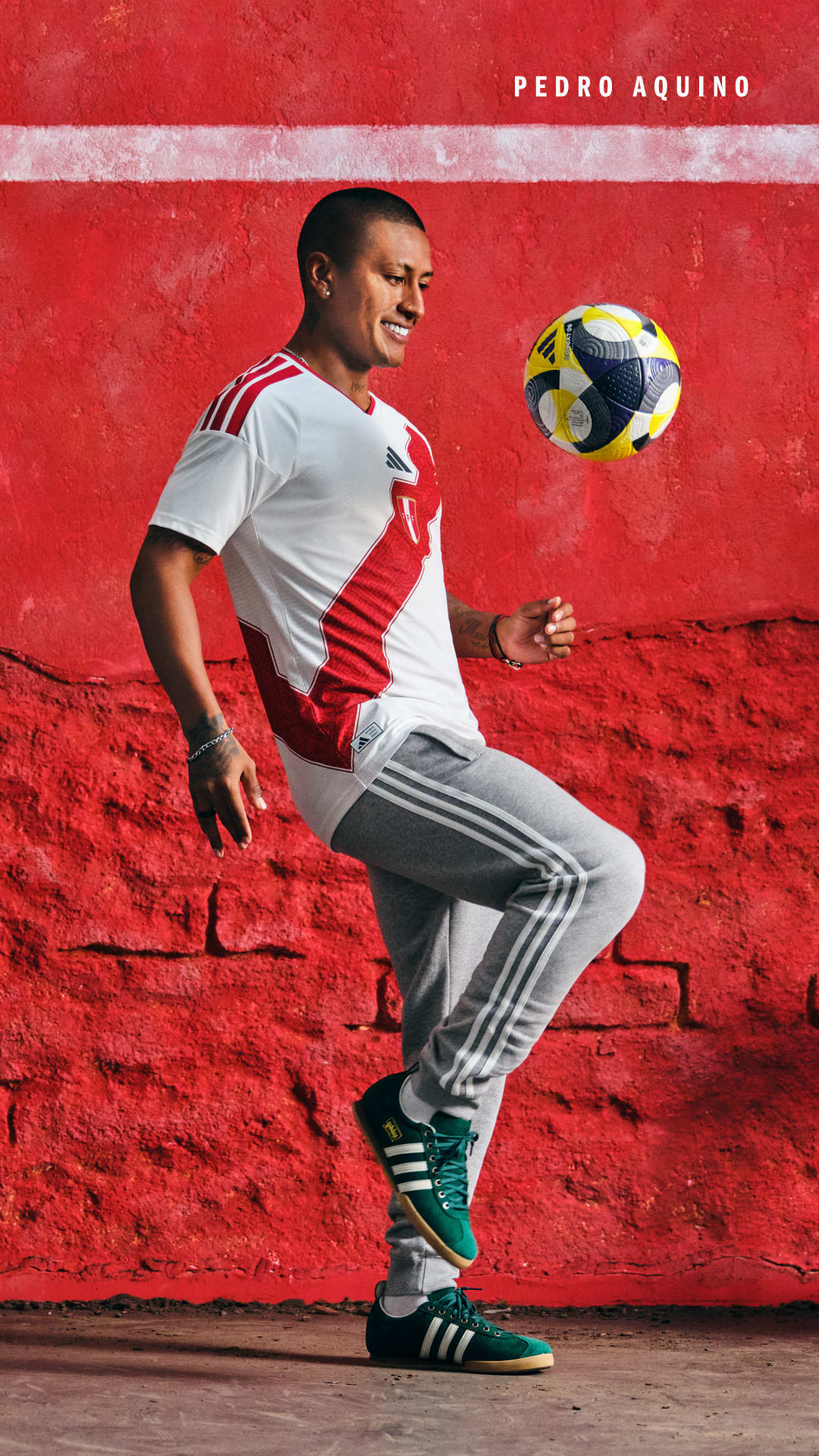 A man in a white jersey and athletic pants stands on a red rocky surface, juggling a soccer ball.