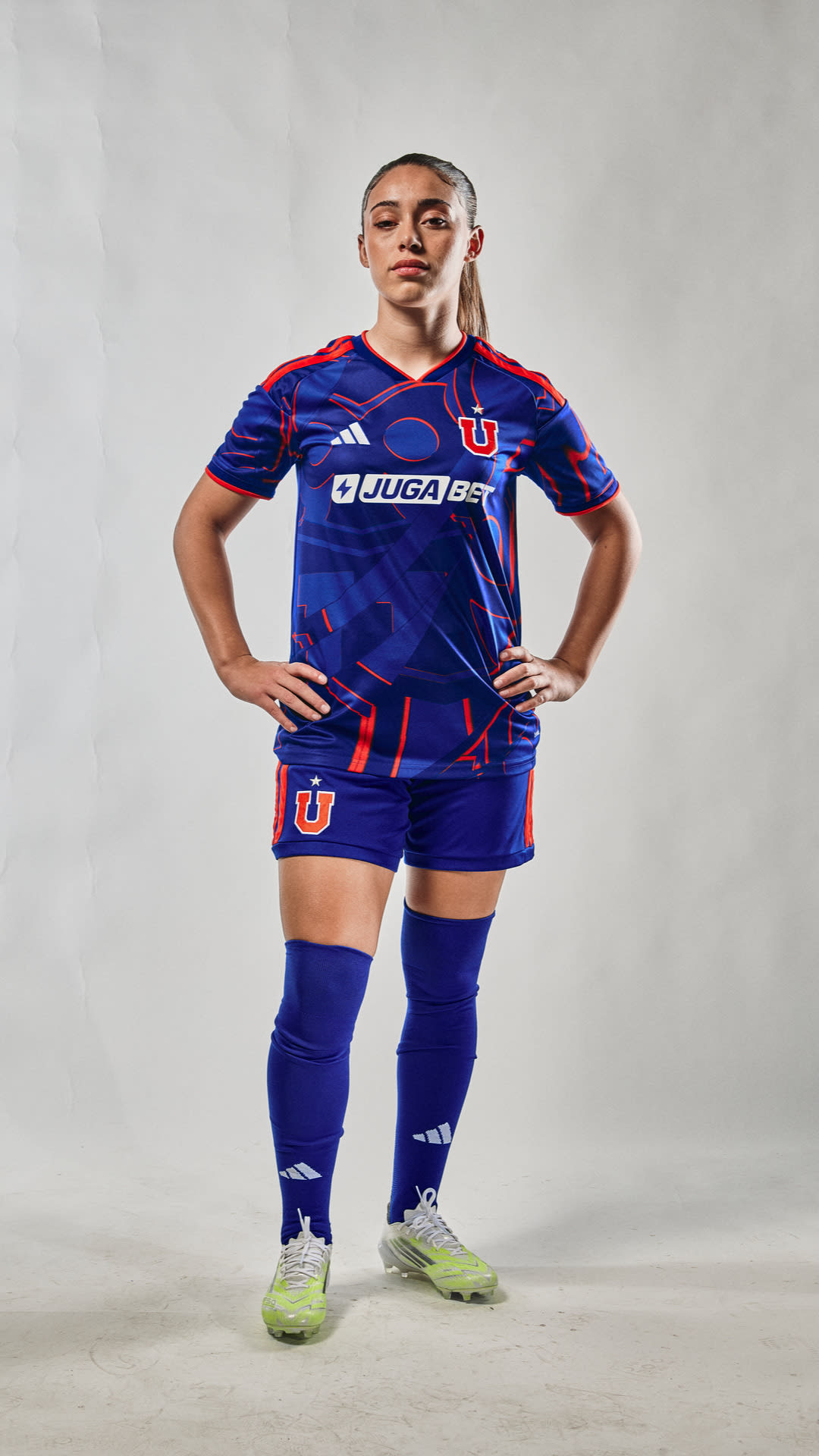 A person wearing a blue and red soccer jersey and shorts, standing with their hands on their hips against a plain gray background.