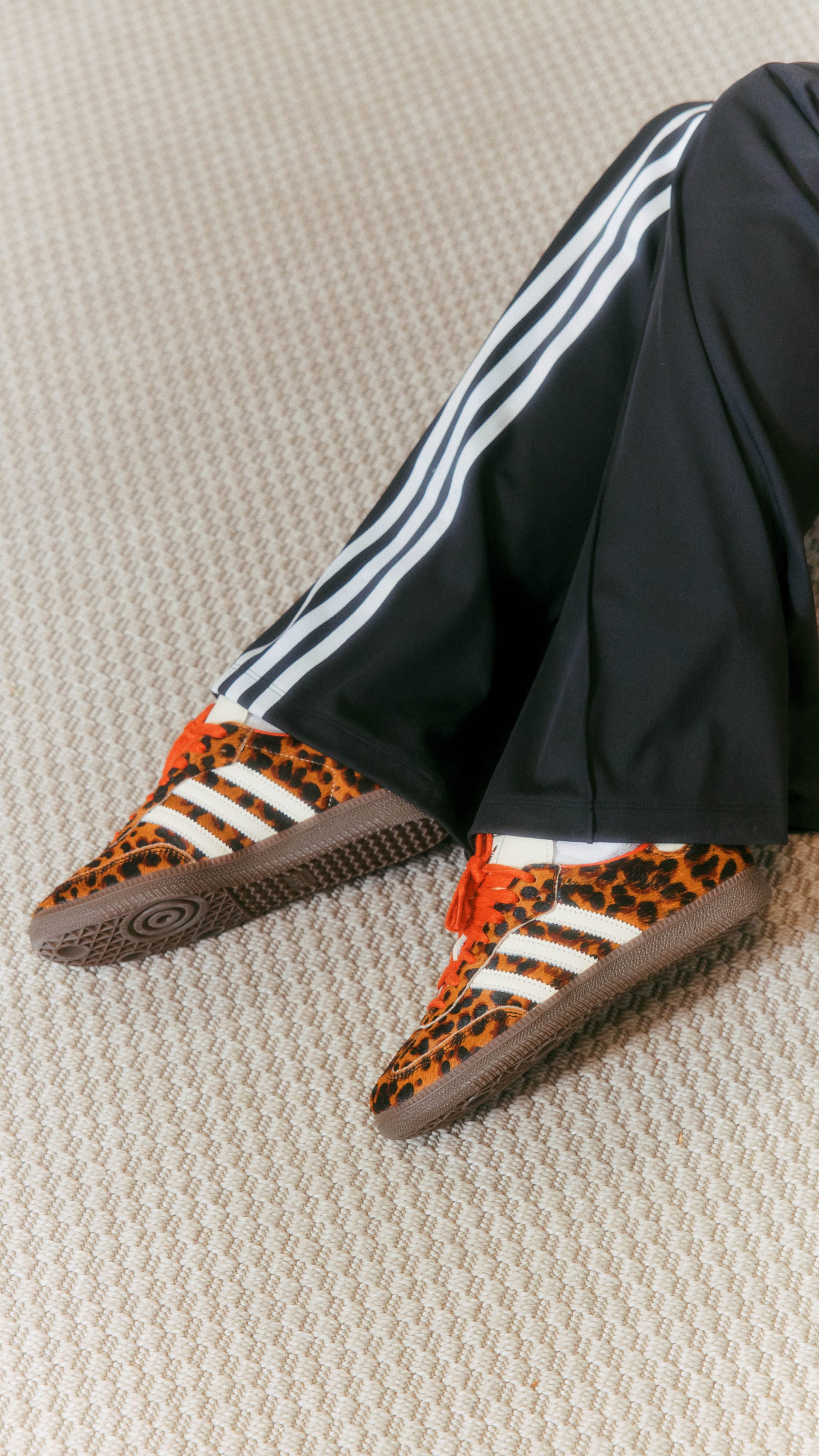 A pair of leopard-print sneakers with black-and-white stripes sits on a beige patterned surface.