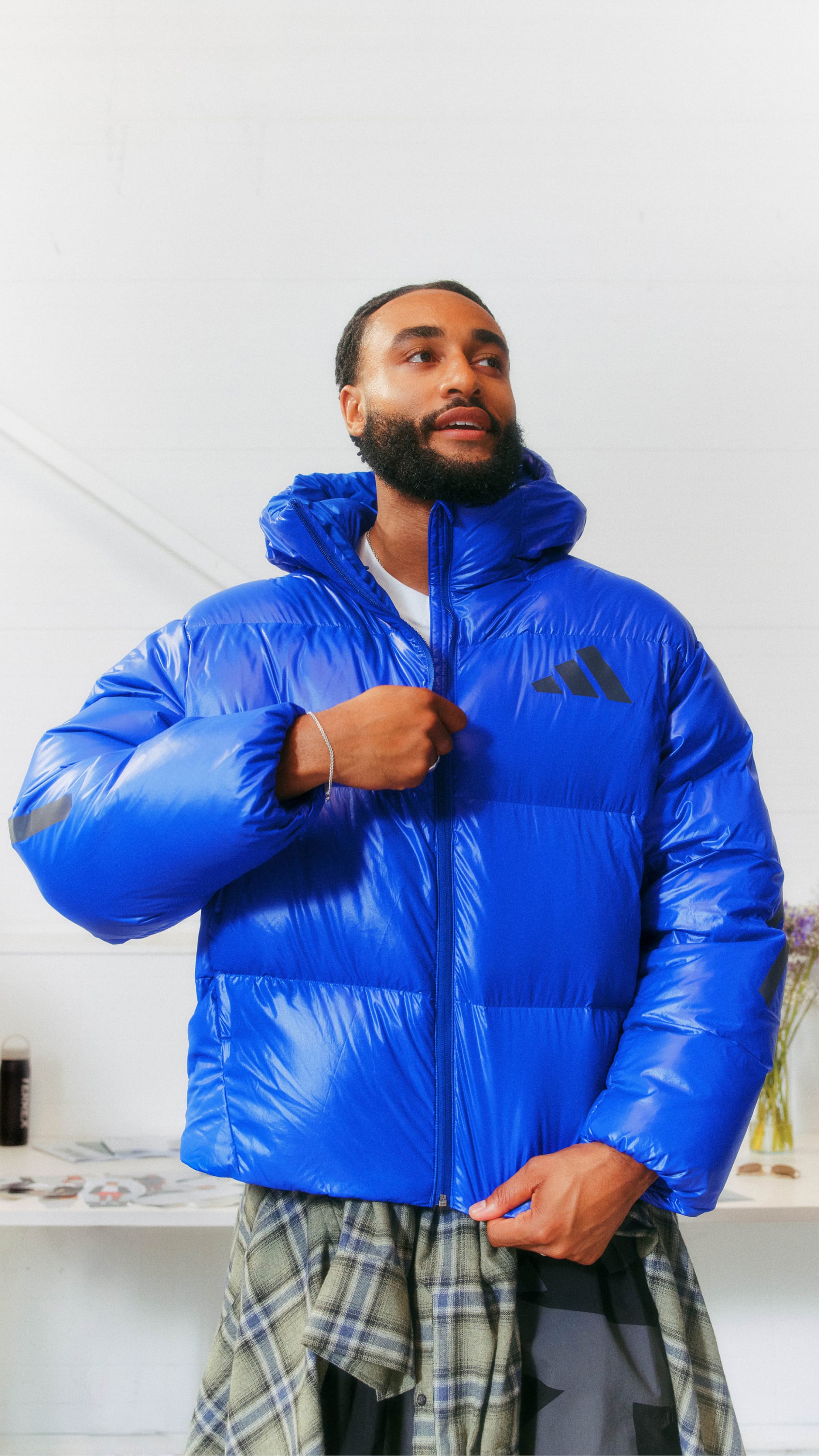 A man wearing a bright blue puffy jacket stands in a room with white walls.