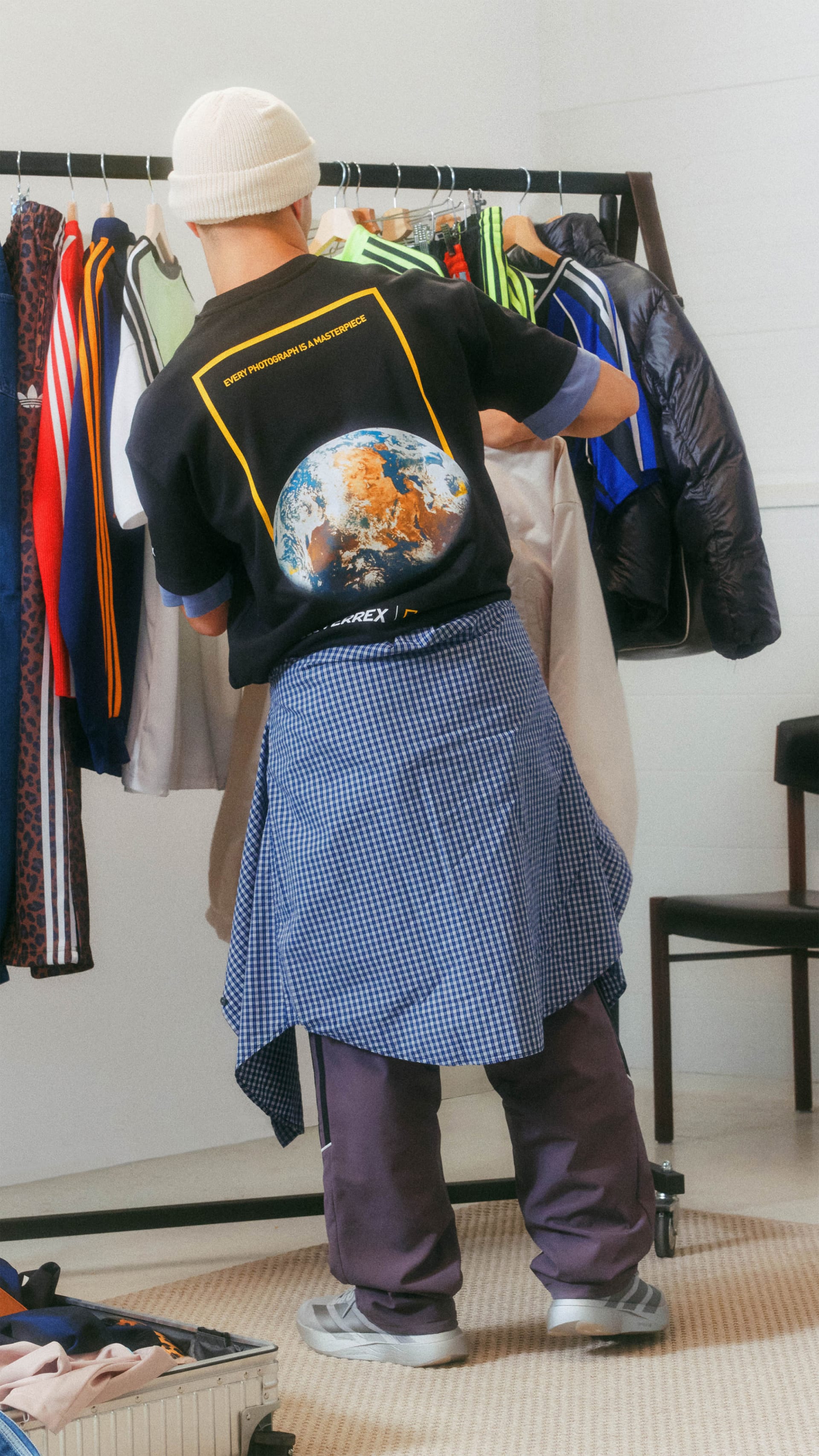 A person wearing a black t-shirt with a globe design is standing in front of a apparel rack filled with various garments.