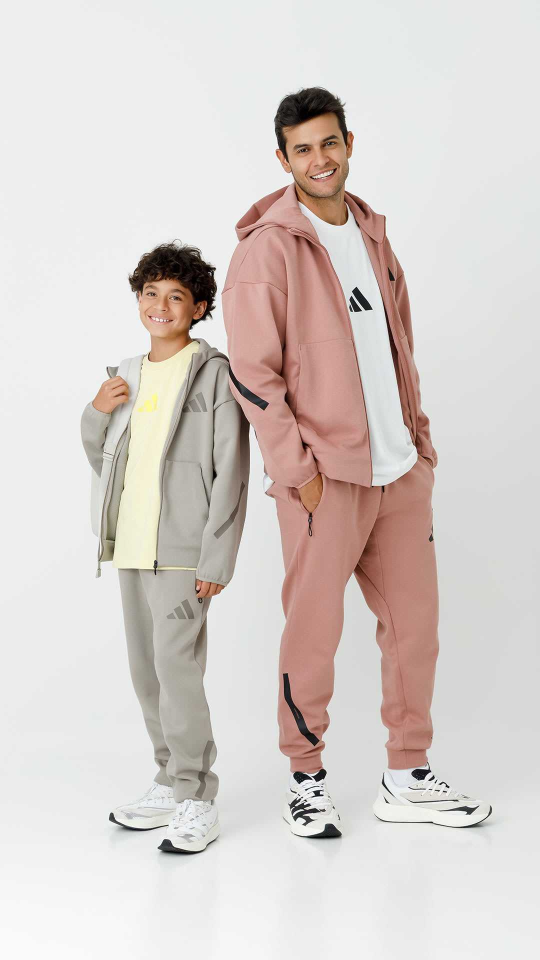 Two individuals, a young boy and a man, are standing together wearing coordinated pastel-colored hoodies and sweatpants. They appear to be posing for a photograph against a plain white background.