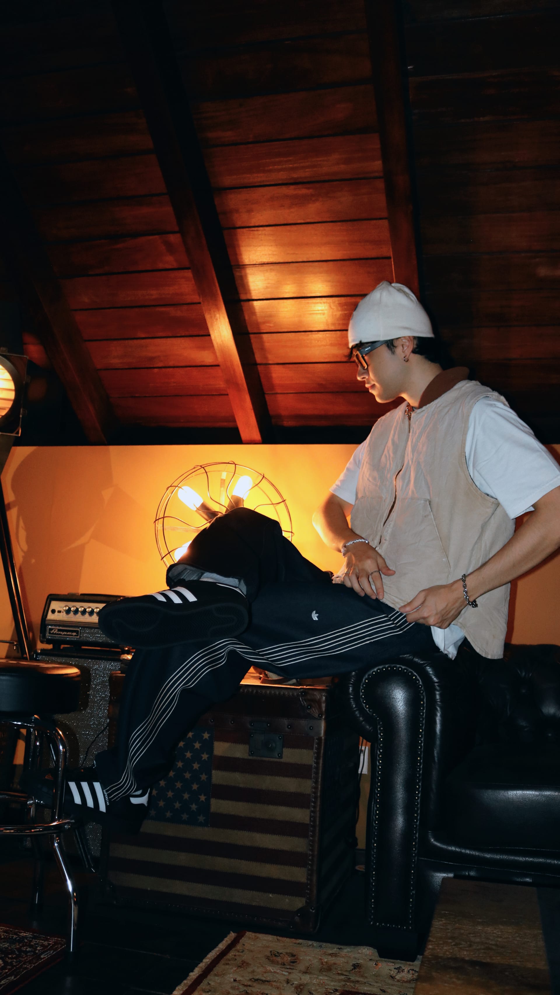 A person in a white shirt and hat is working on a motorcycle in a dimly lit garage with wooden beams and a warm, orange-toned lighting.
