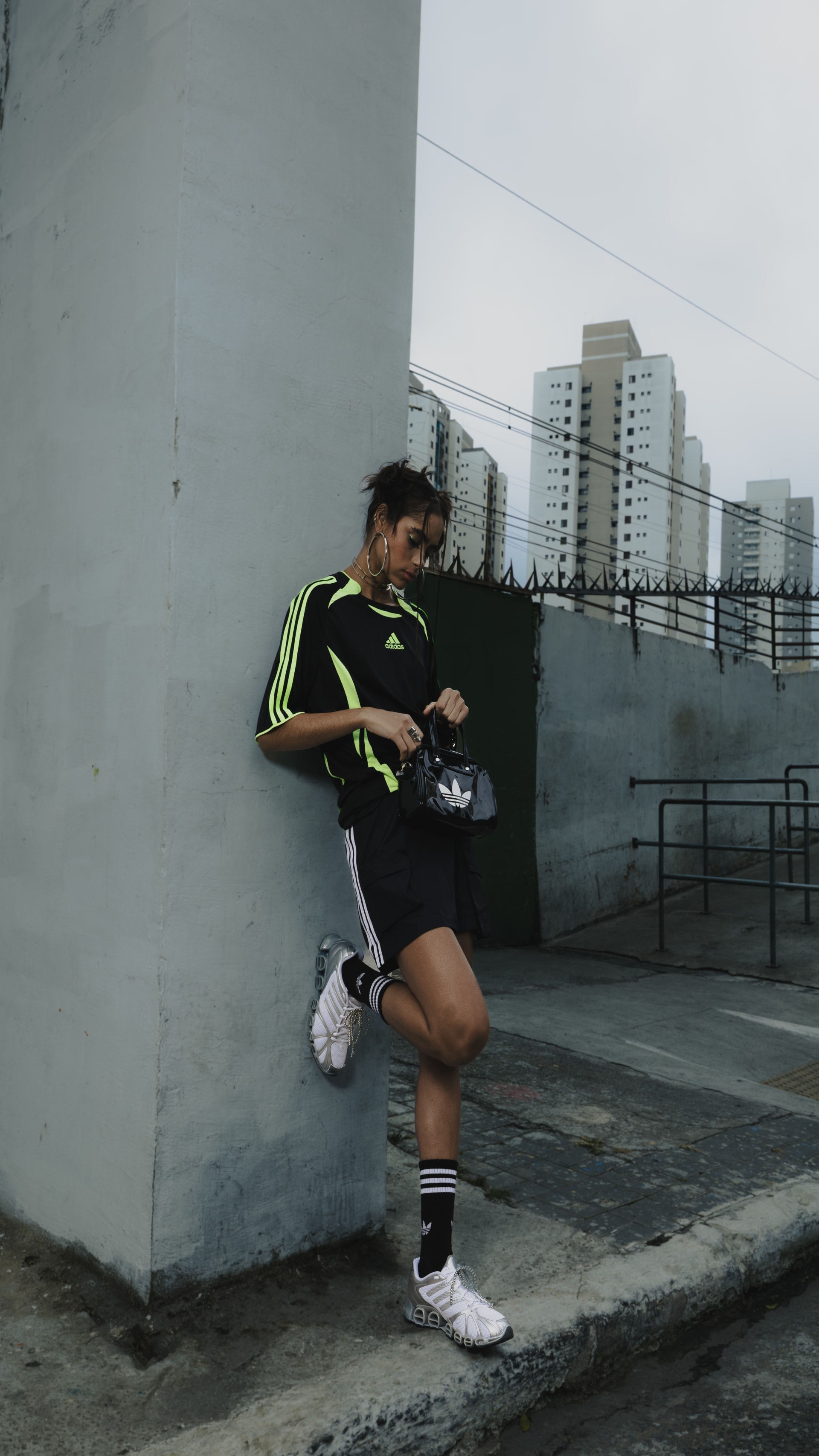 A person in athletic clothing stands against a wall with a cityscape visible in the background.