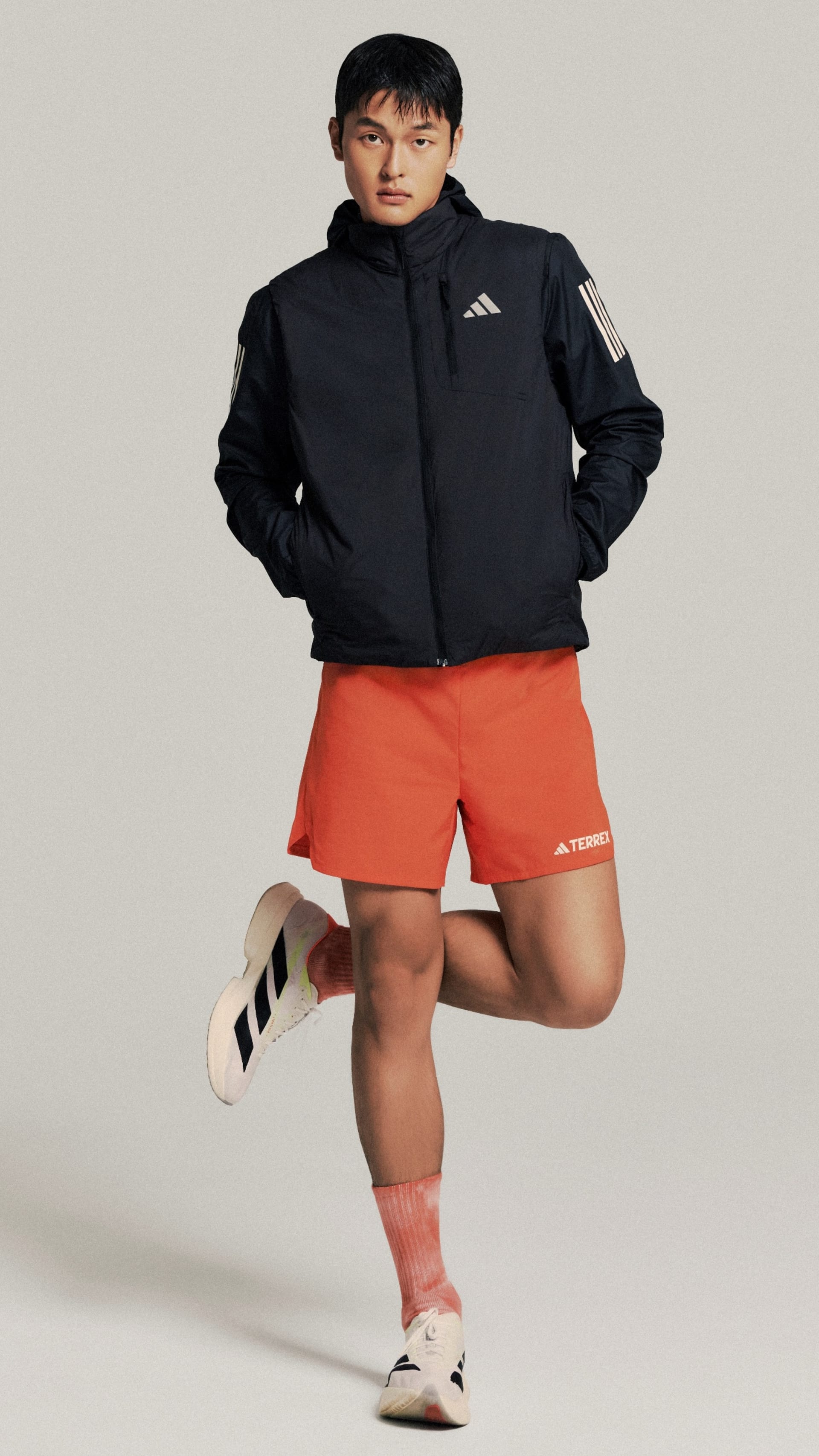 A person wearing a black jacket and orange shorts, standing against a plain background.