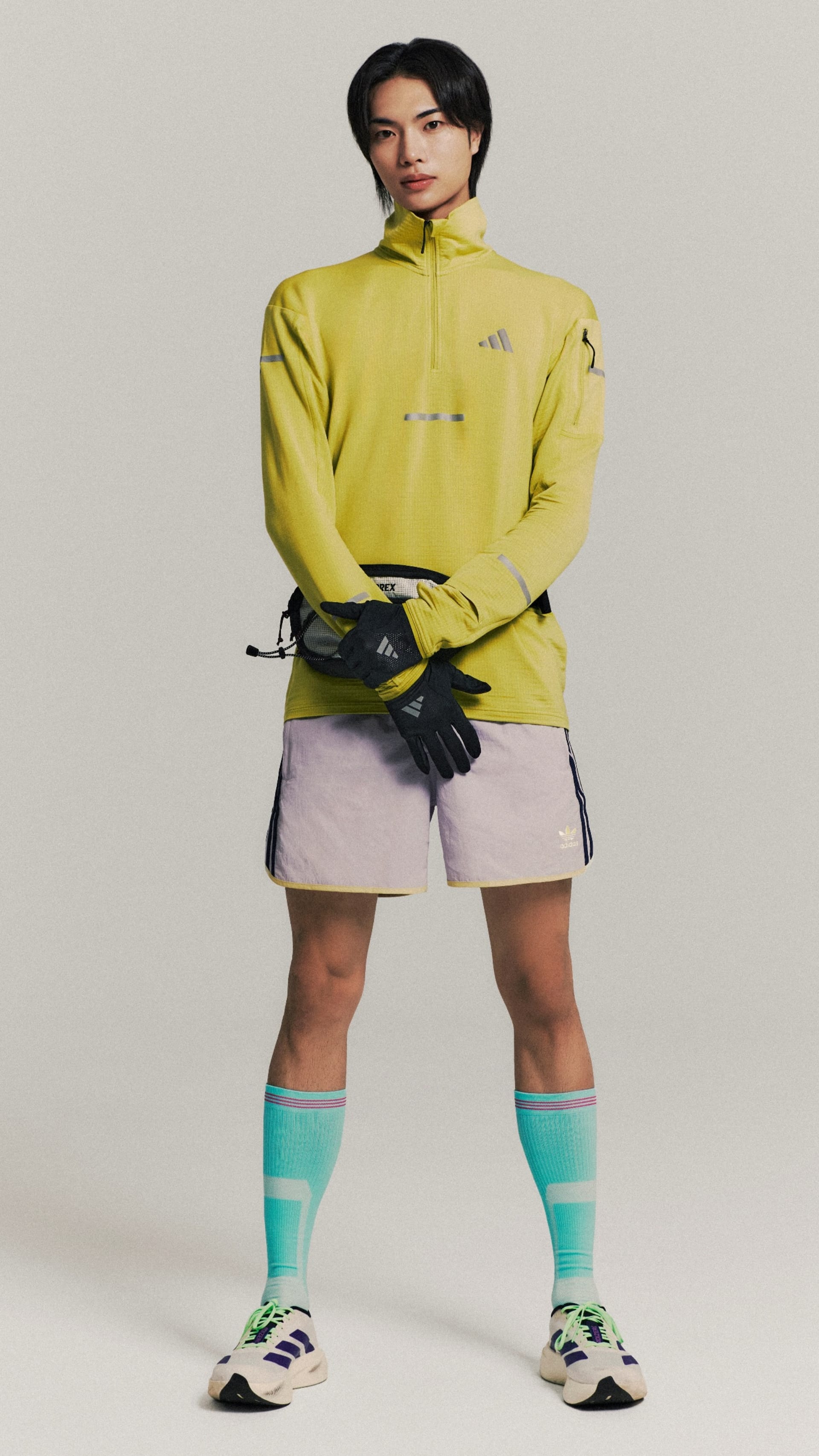 A person wearing a bright yellow jacket, shorts, and colorful socks stands against a plain background.