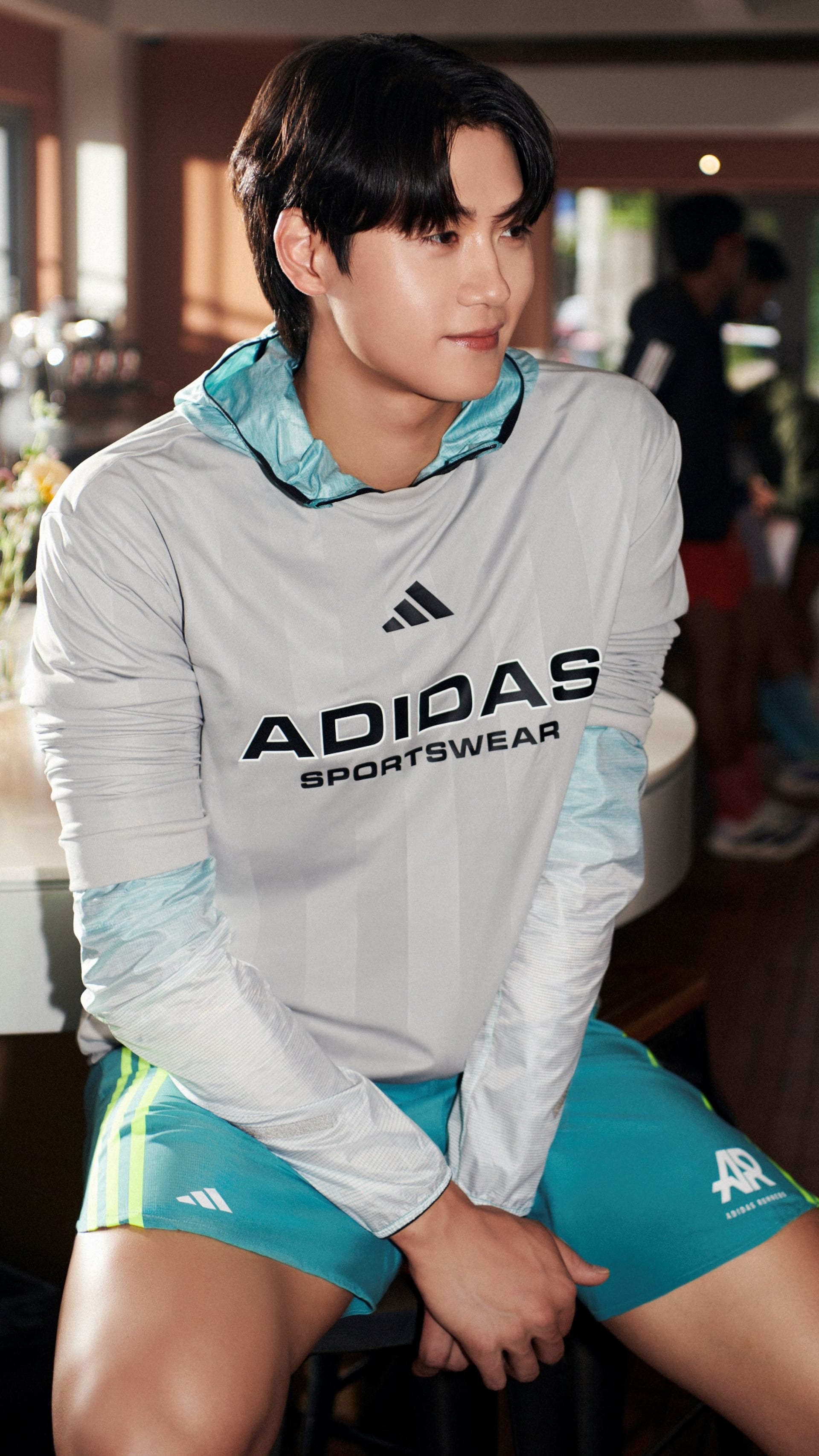A young person wearing an Adidas sportswear outfit is standing in what appears to be a commercial or retail setting, with a blurred background suggesting an indoor environment.