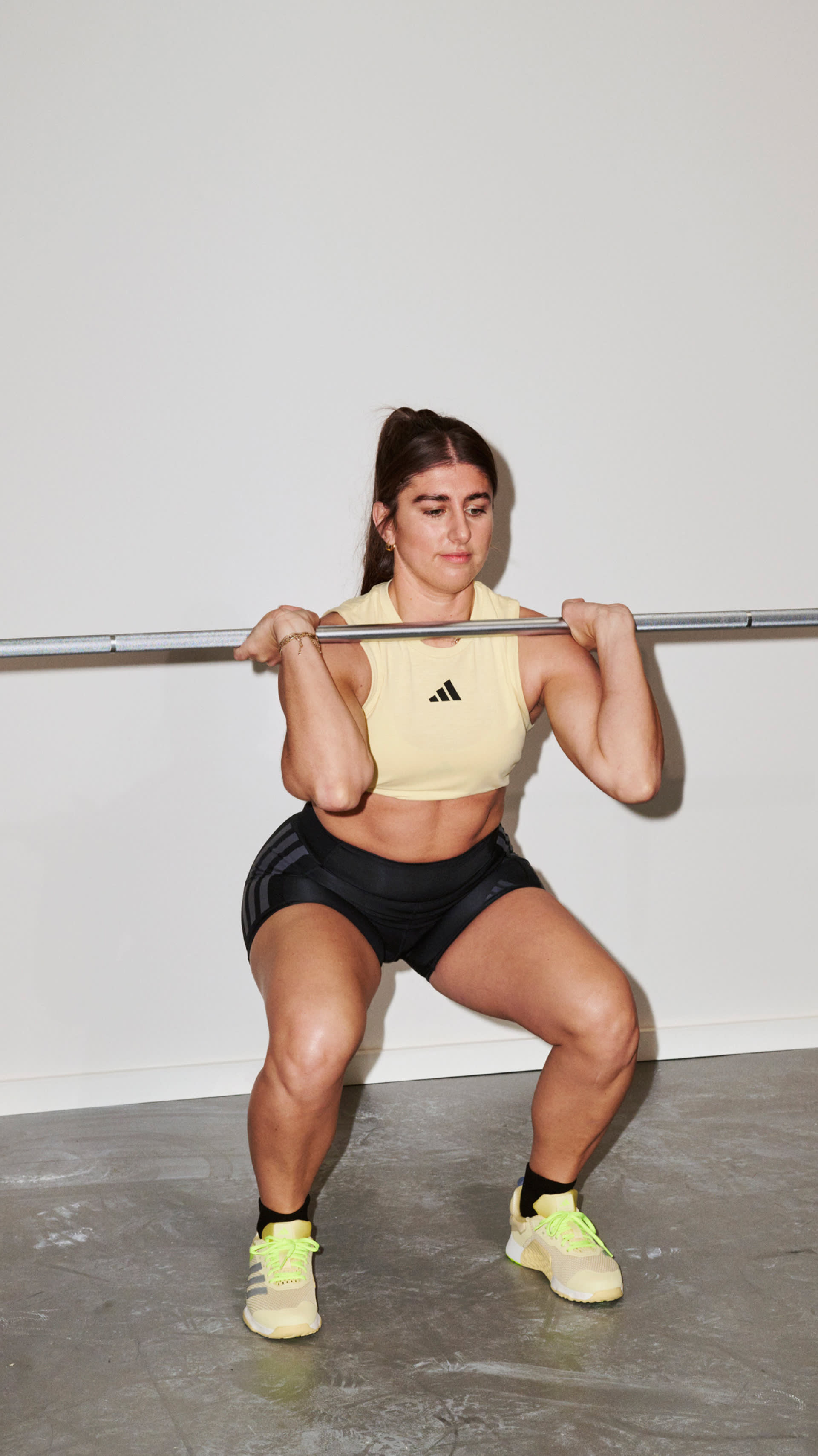 A woman in athletic clothing is performing a squat exercise while holding a barbell in a gym setting.