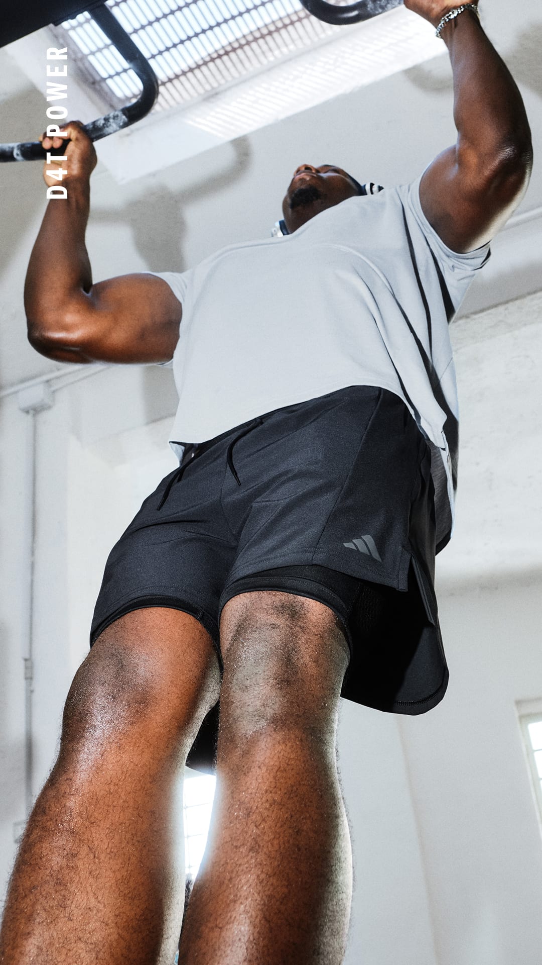 Das Bild zeigt eine Person, die eine Klimmzugübung auf einem Fitnessgerät durchführt. Im Hintergrund sind eine weiße Wand und ein Metallrahmen zu sehen.