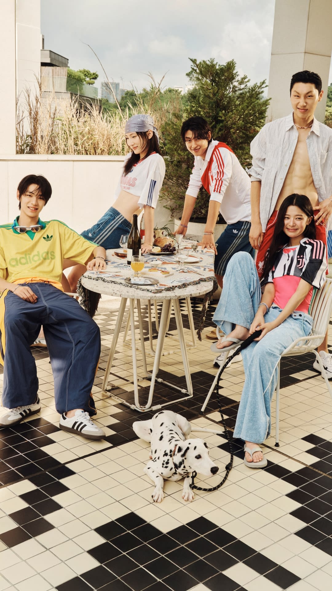 A group of young people enjoying a casual outdoor gathering, with a dog in the foreground and a tiled patio area in the background.