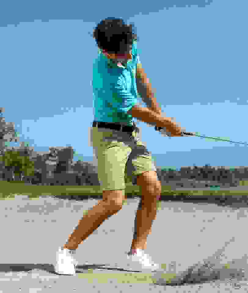 Joaquin Neimann swinging a golf club in a sand trap wearing adidas clothing.