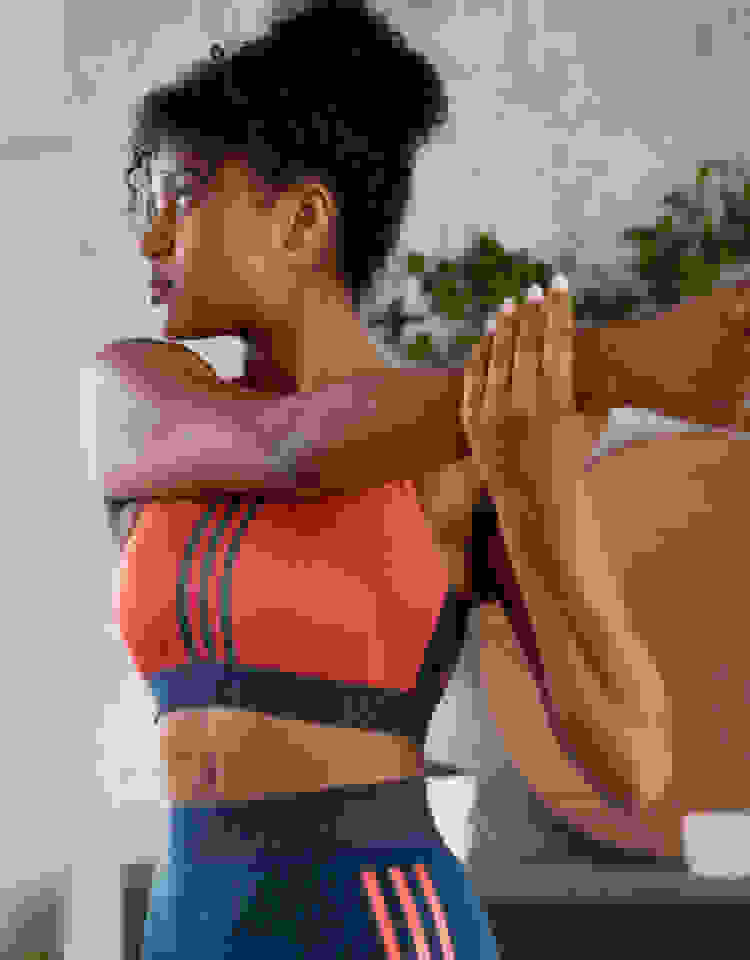 A woman wearing a red adidas bra looks over her shoulder as she stretches her arm.