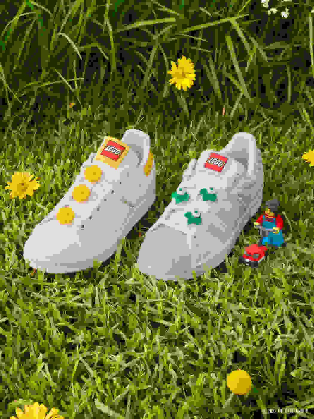 adidas Originals LEGO Superstar and Stan Smith shoes, nestled in meadow grass with LEGO lawnmower minifigure