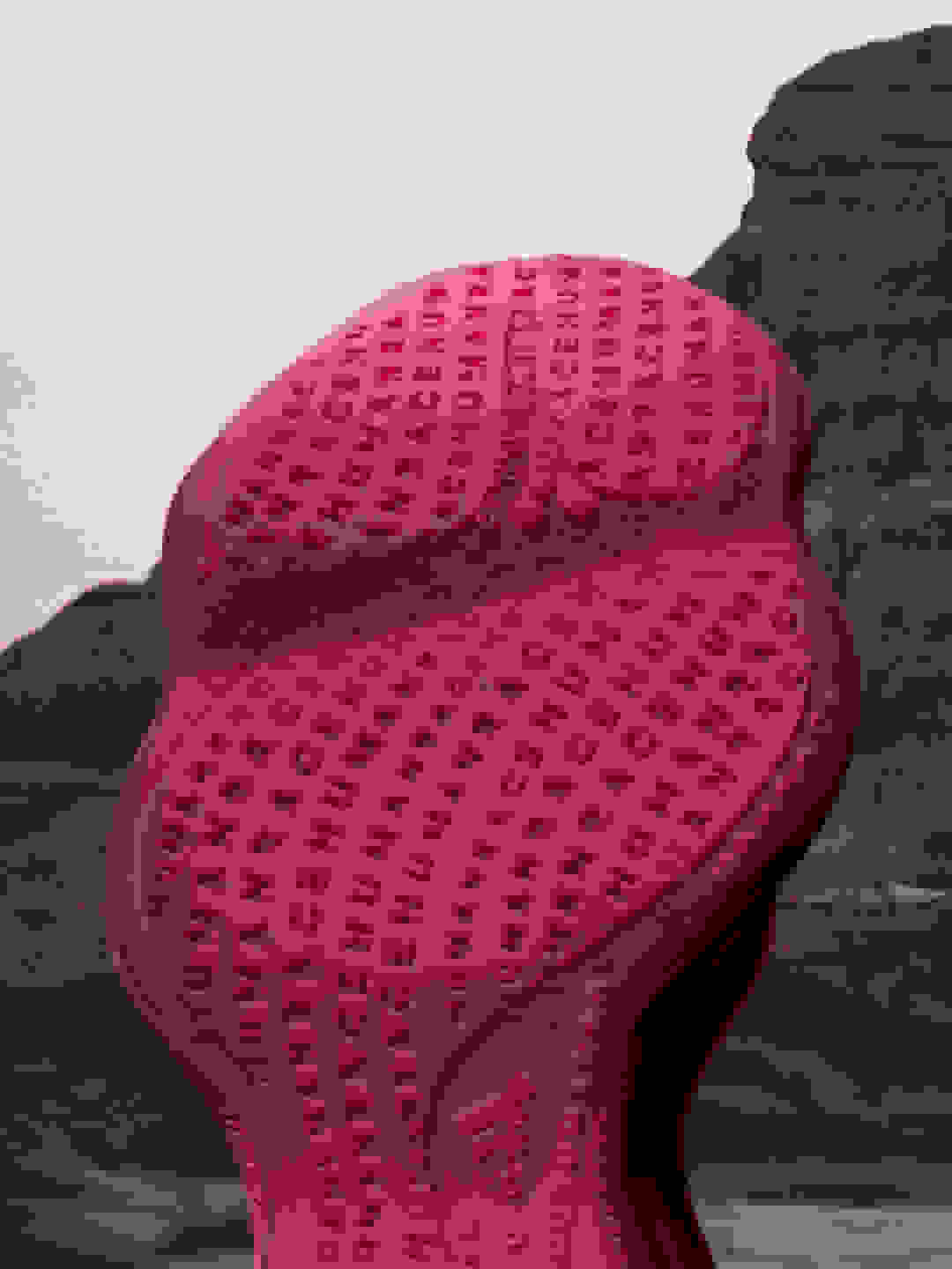 The outsole of a burgundy Humanrace Sičhona shoe against the backdrop of a mountain and tinted sky.