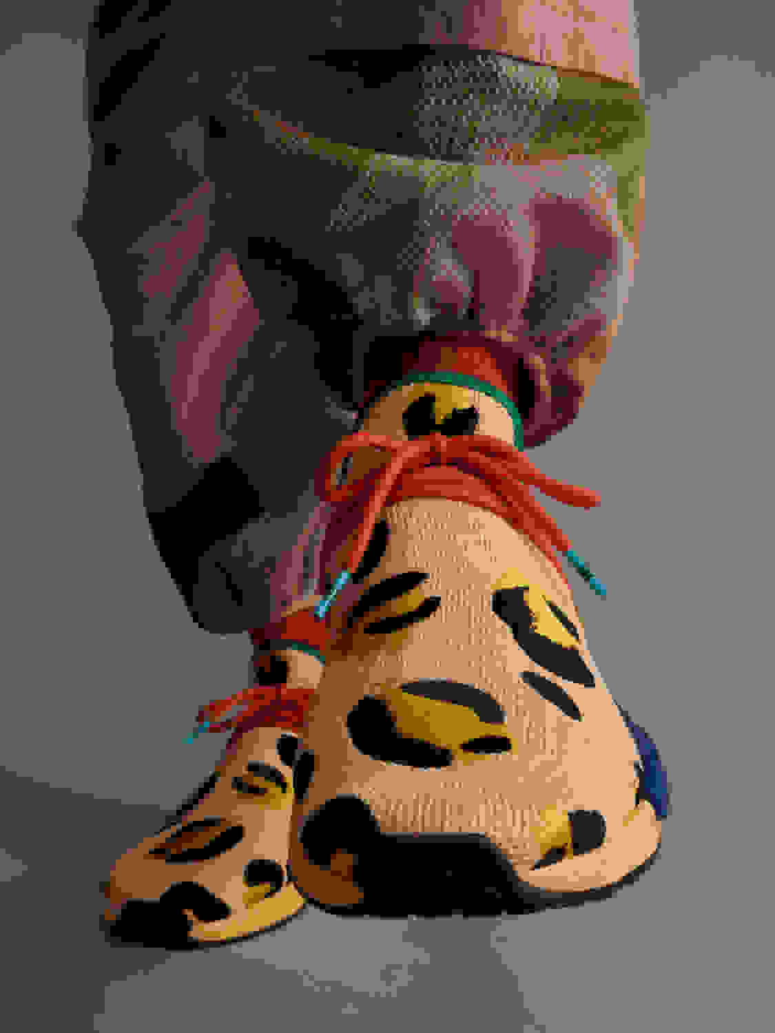 Front view of amber animal print shoe, as model wearing amber pants puts shoe on.