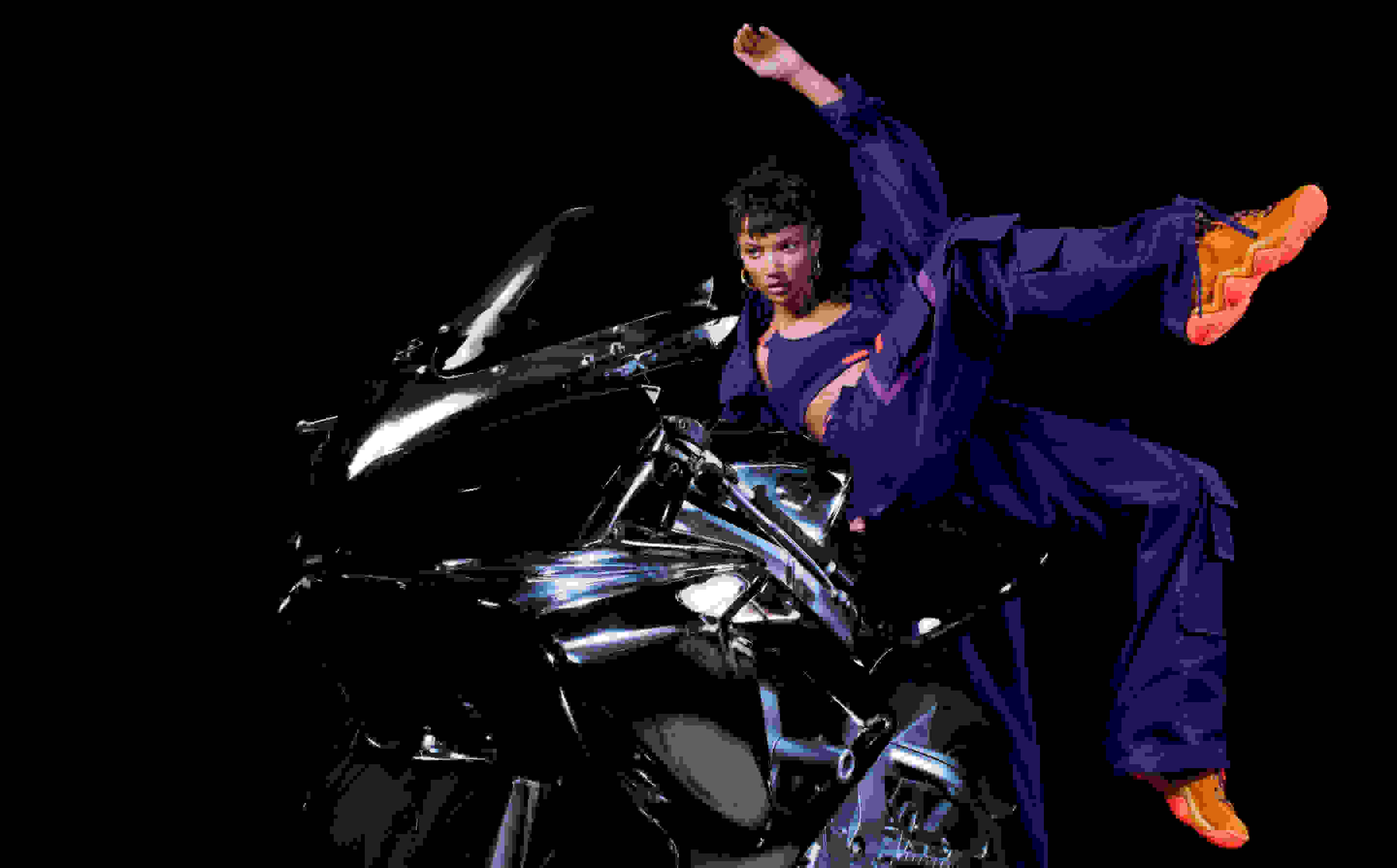 A model is photographed posing on a motorbike in the adidas x IVY PARK collection against a black backdrop.