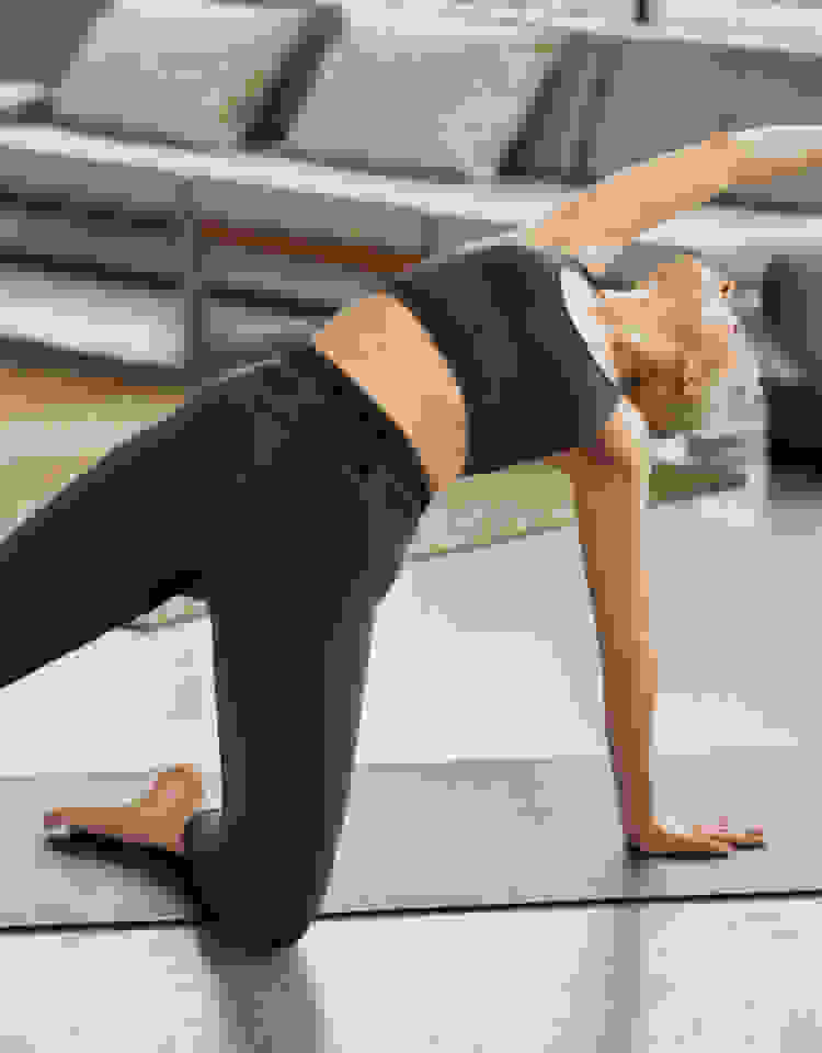A woman in a black bra and tights stretches in a yoga pose on a mat.