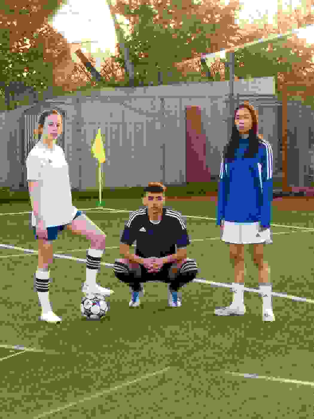 Image of 3 players, 2 females, one male posing on the pitch, kits on, female on the left hand side has the ball.