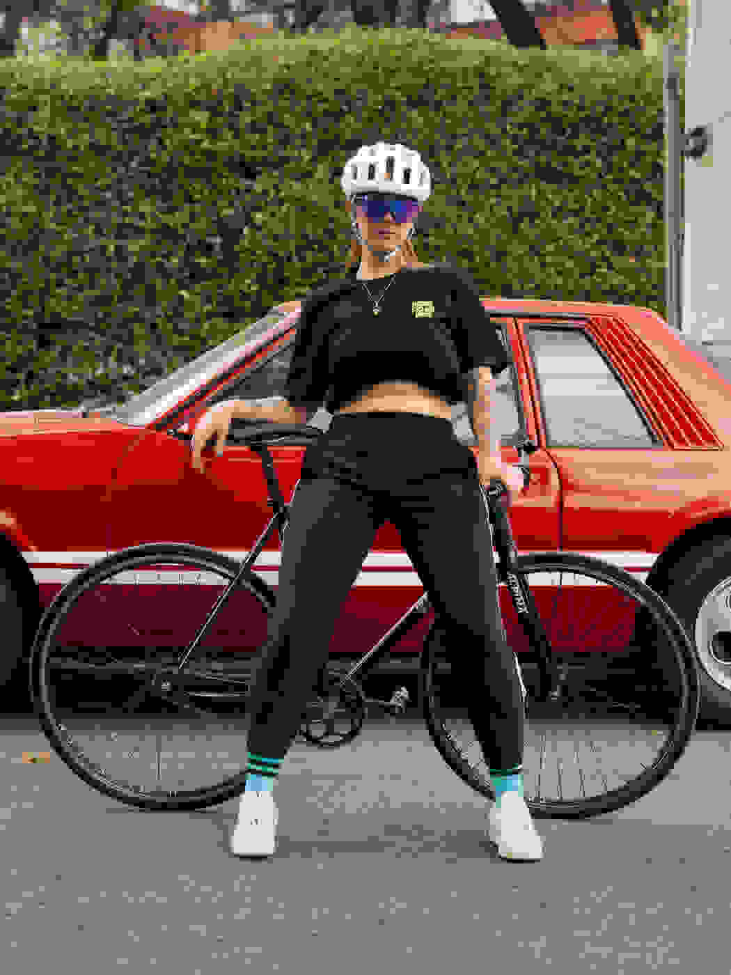 A woman stood in front of a bicycle with a red car in the background