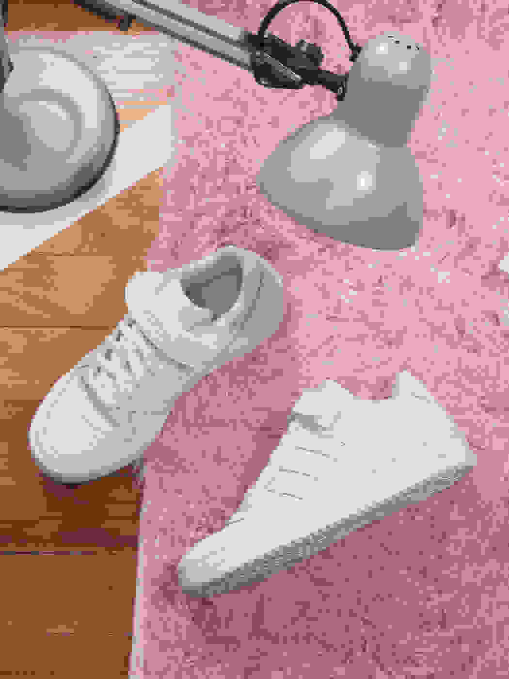 A pair of white sneakers on pink carpet
