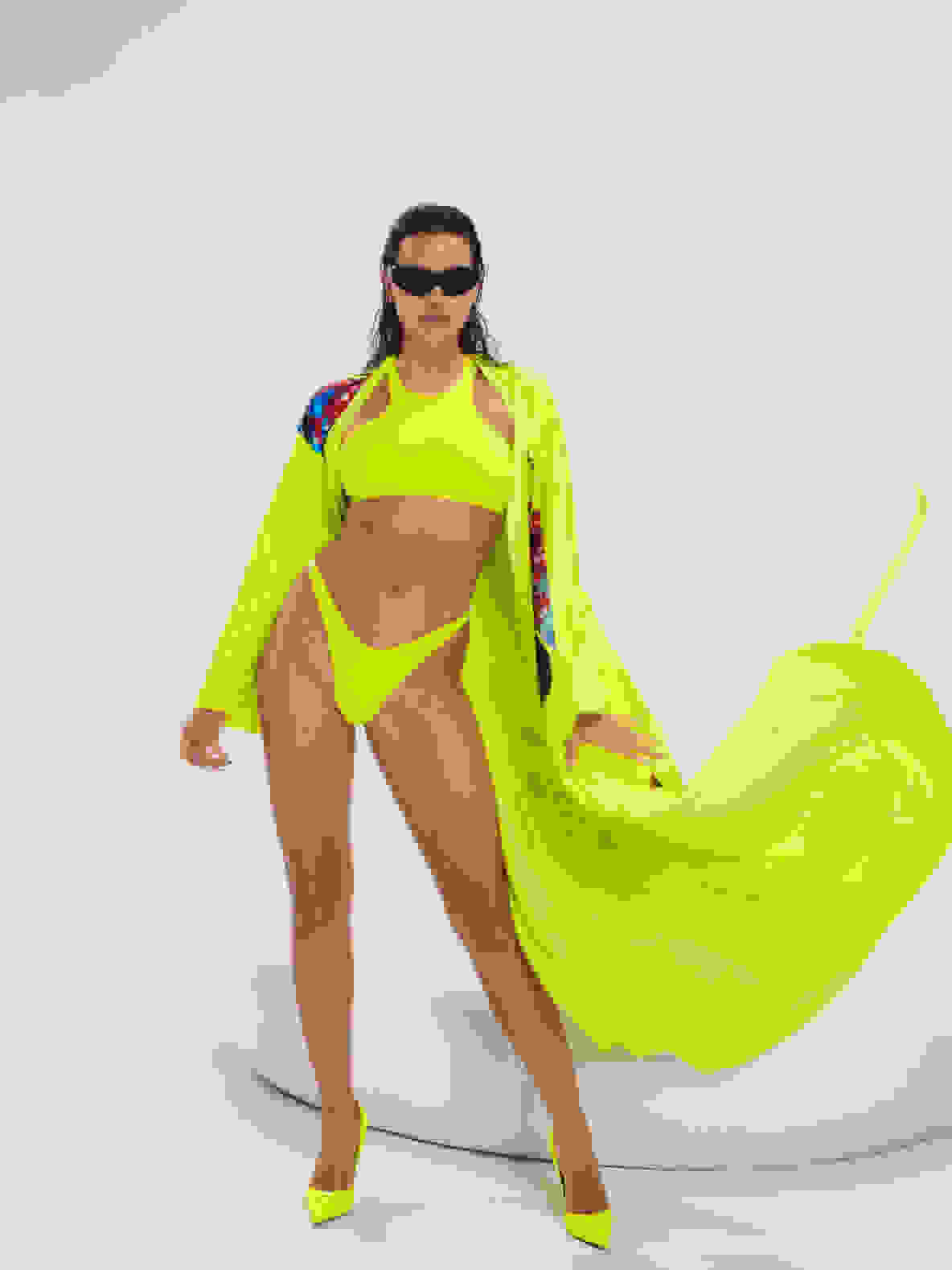 Model in solar yellow outfit stands on black background.