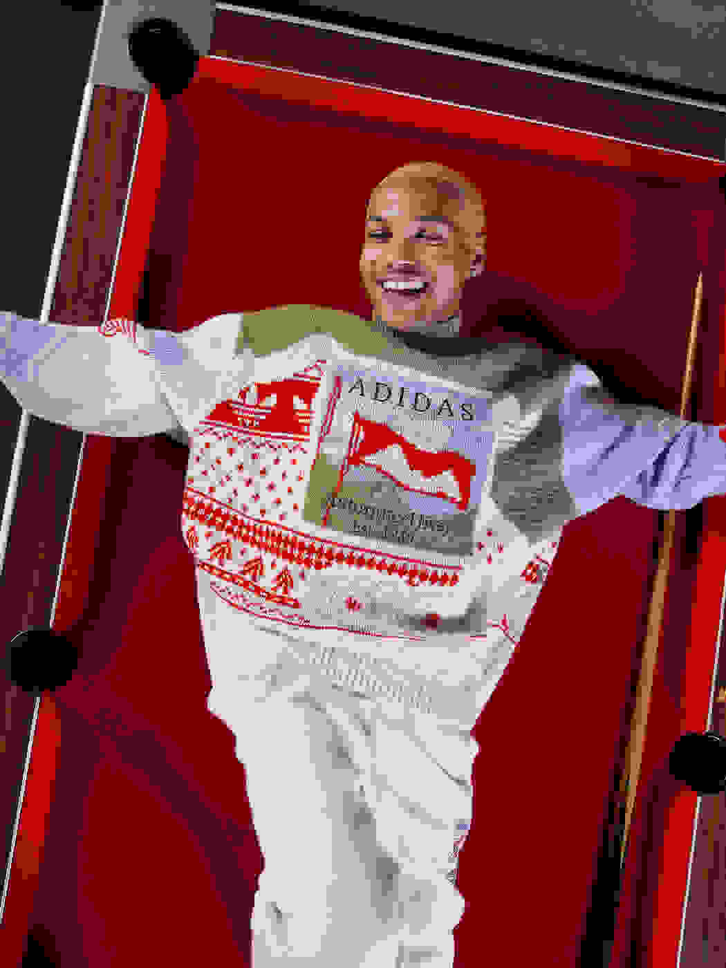 Smiling man in Christmas jumper sits on side of a pool table whilst tying shoelaces.